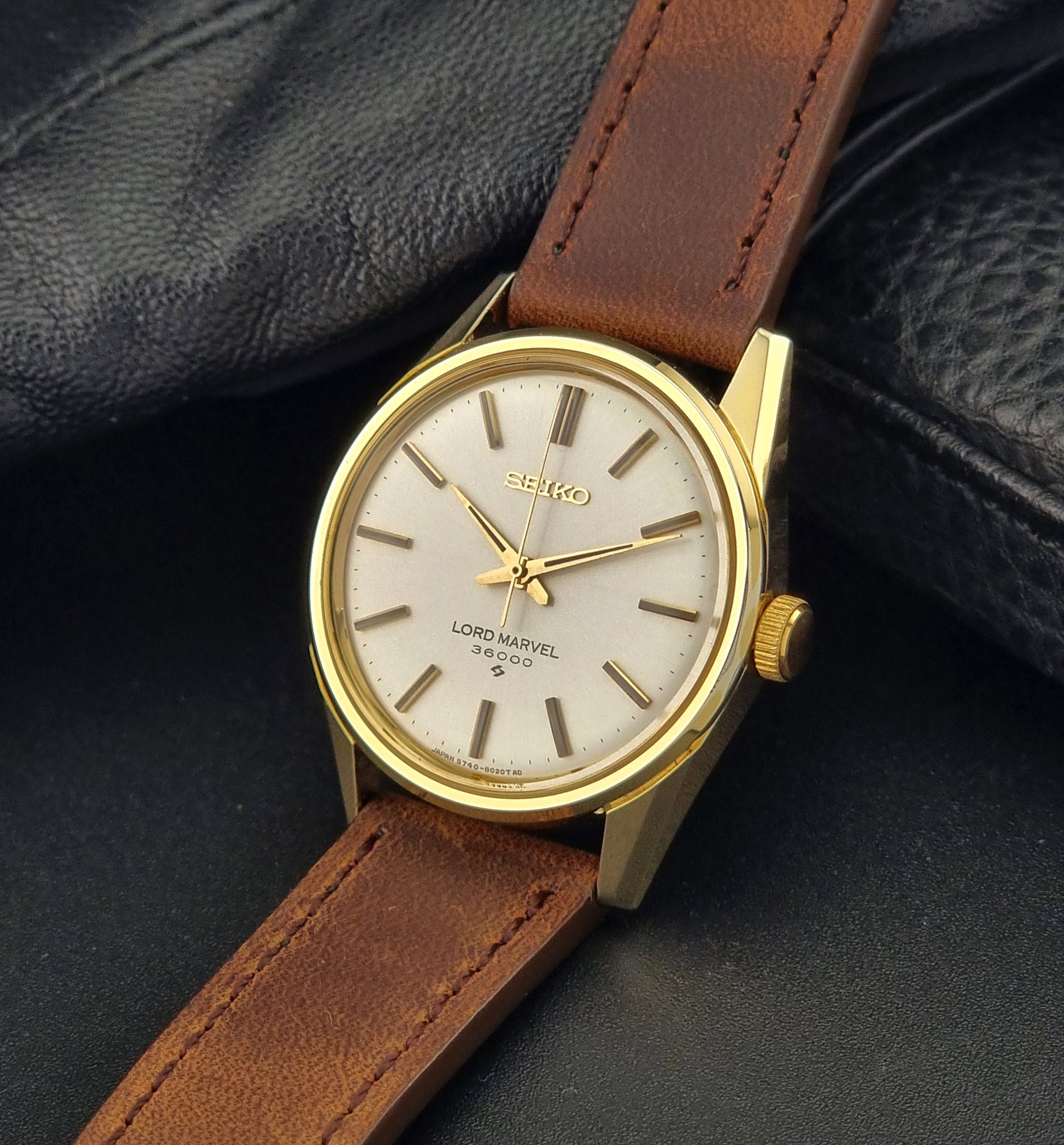 Vintage Seiko Lord Marvel 5740-8000 gold watch with a brown leather strap on a dark gray background crown view