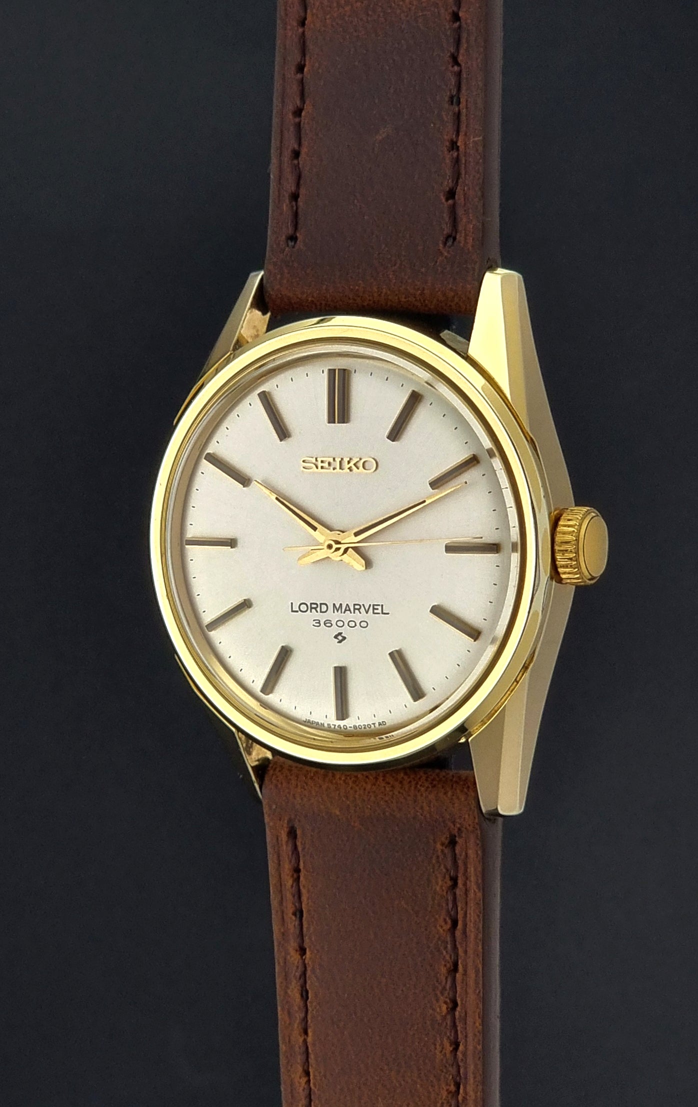Vintage Seiko Lord Marvel 5740-8000 gold watch with a brown leather strap on a dark gray background crown profile