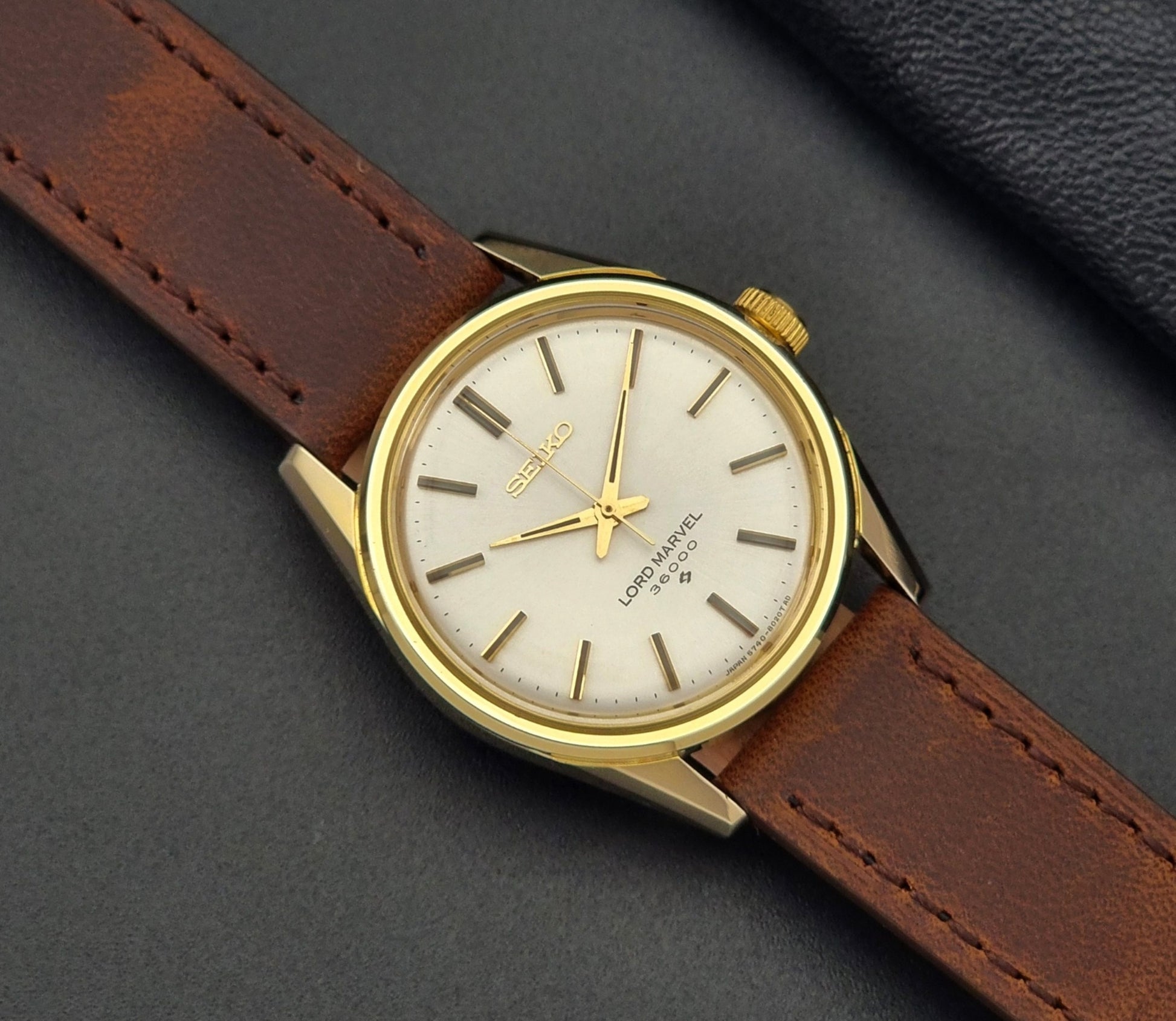 Vintage Seiko Lord Marvel 5740-8000 gold watch with a brown leather strap on a dark gray background