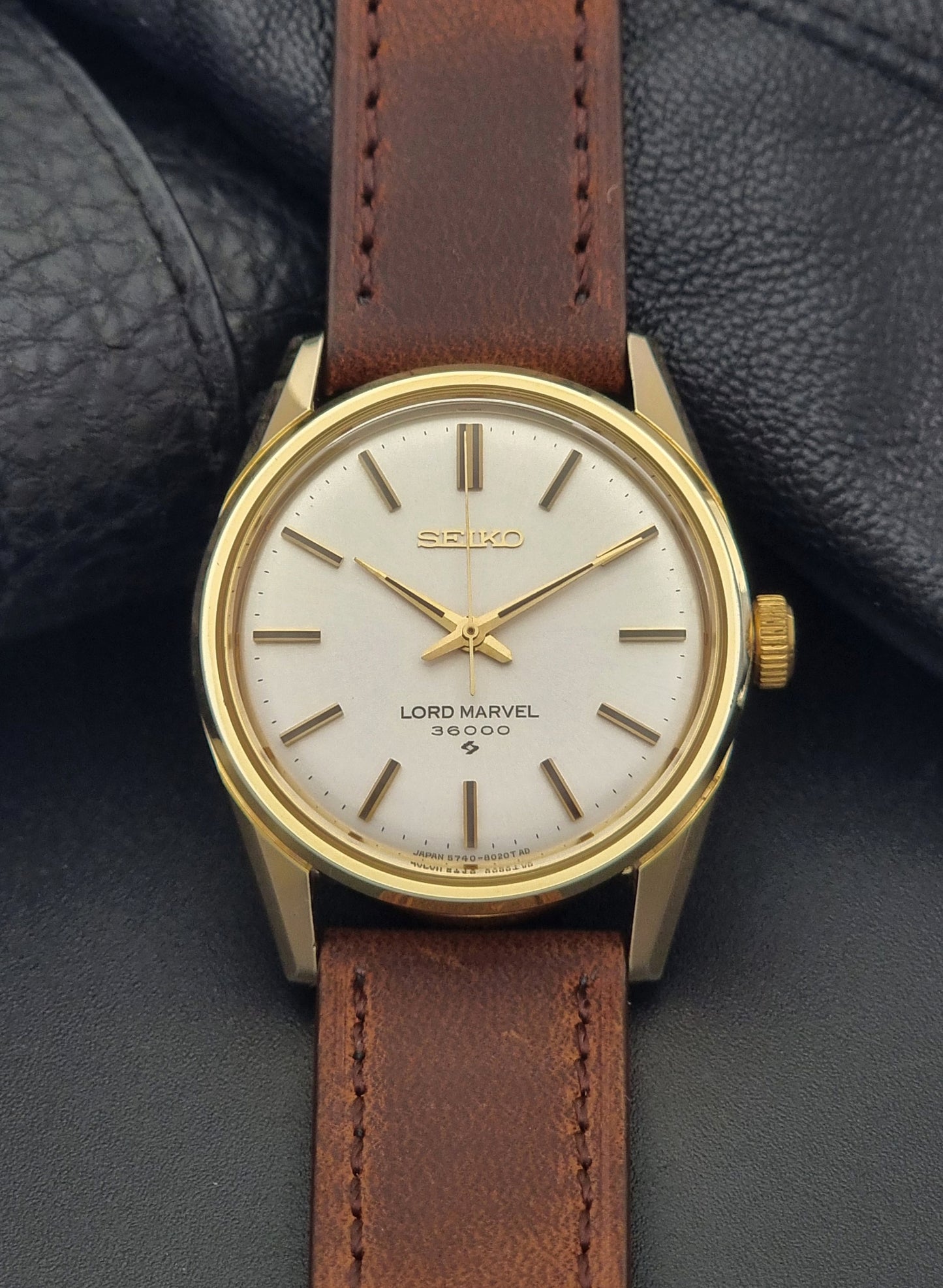 Vintage Seiko Lord Marvel 5740-8000 gold watch with a brown leather strap on a dark gray background front