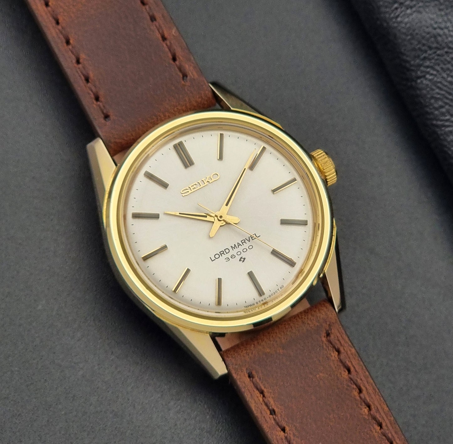 Vintage Seiko Lord Marvel 5740-8000 gold watch with a brown leather strap on a dark gray background close up