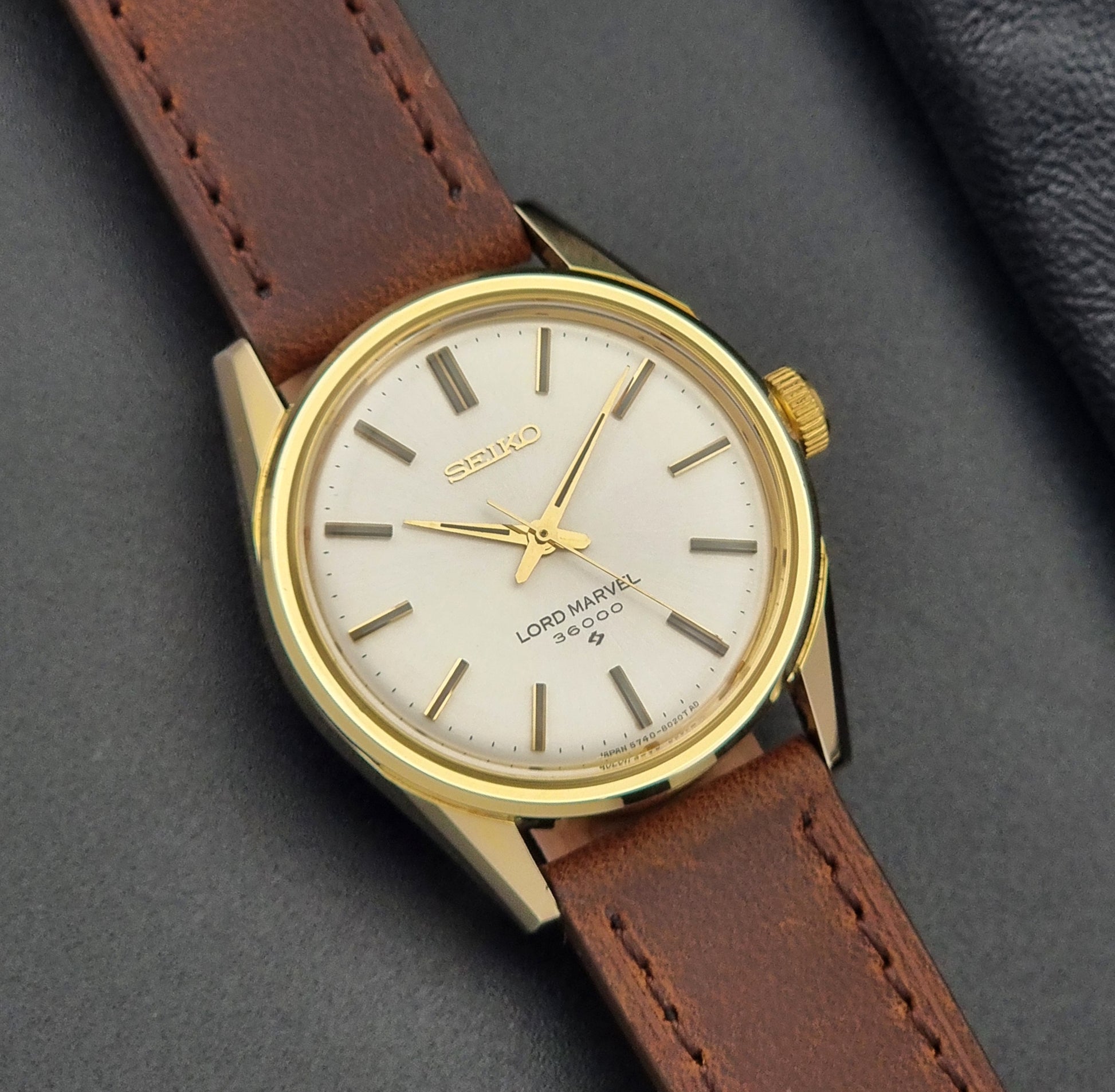 Vintage Seiko Lord Marvel 5740-8000 gold watch with a brown leather strap on a dark gray background close up