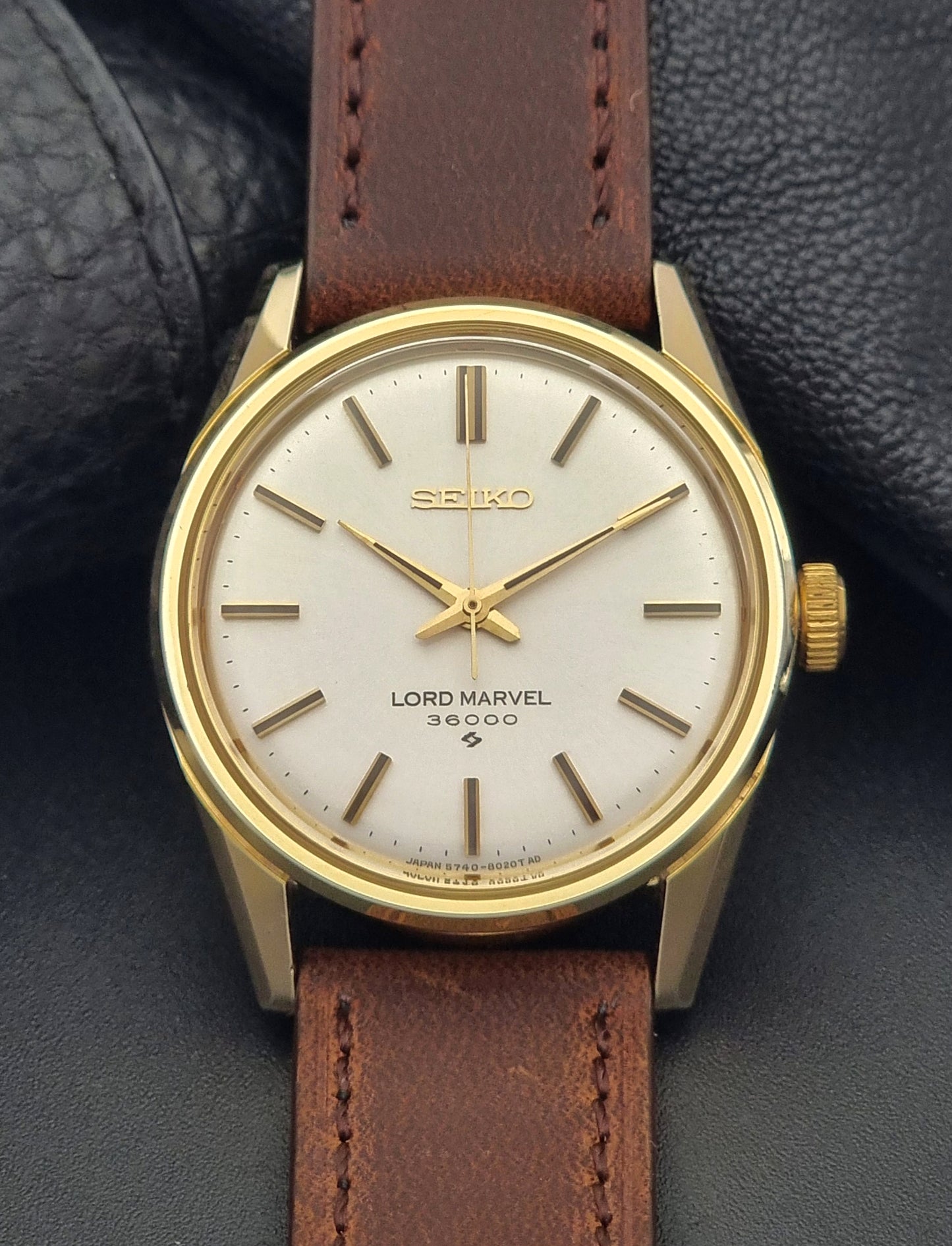 Vintage Seiko Lord Marvel 5740-8000 gold watch with a brown leather strap on a dark gray background close up dial