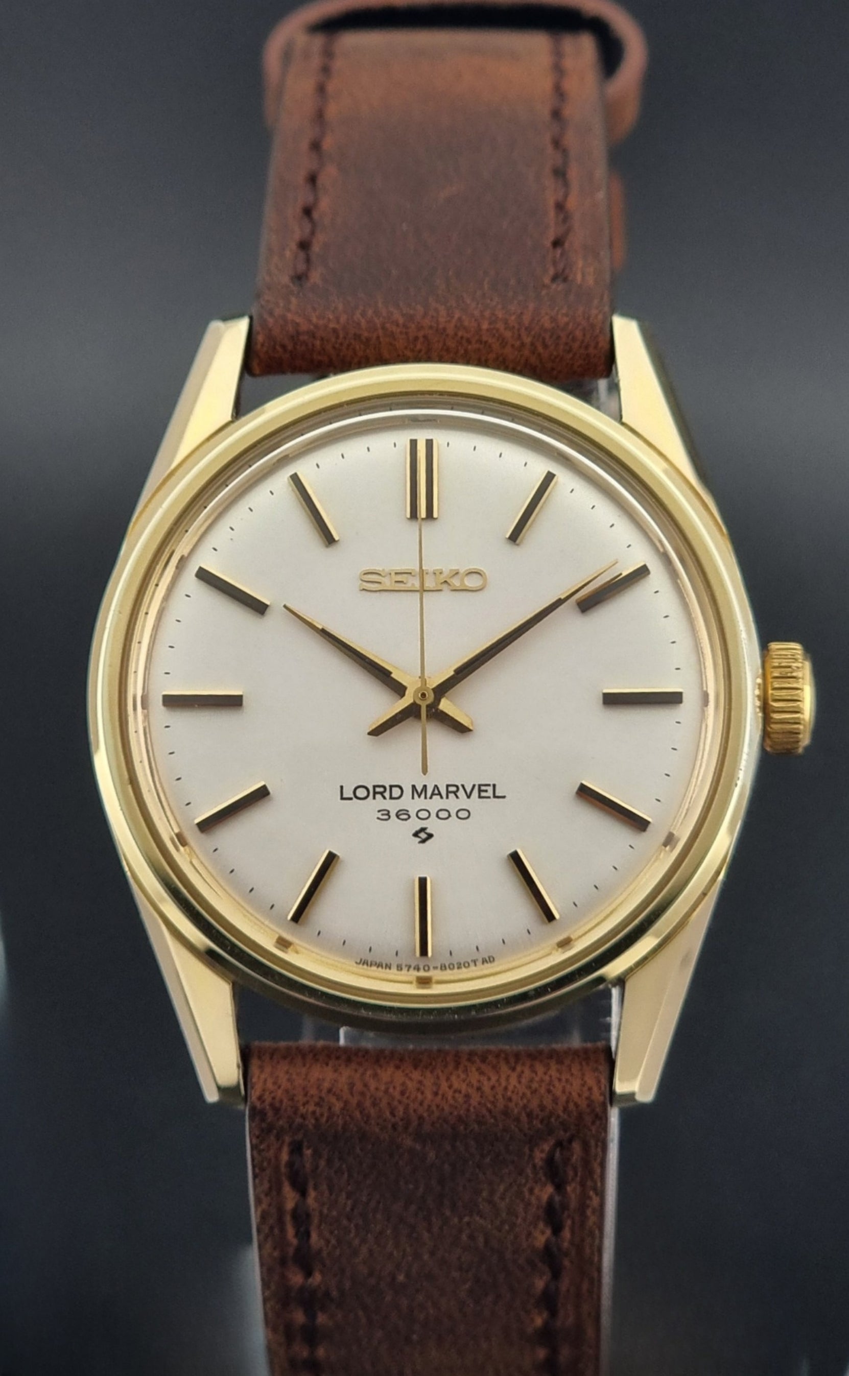 Vintage Seiko Lord Marvel 5740-8000 gold watch with a brown leather strap on a dark gray background front view