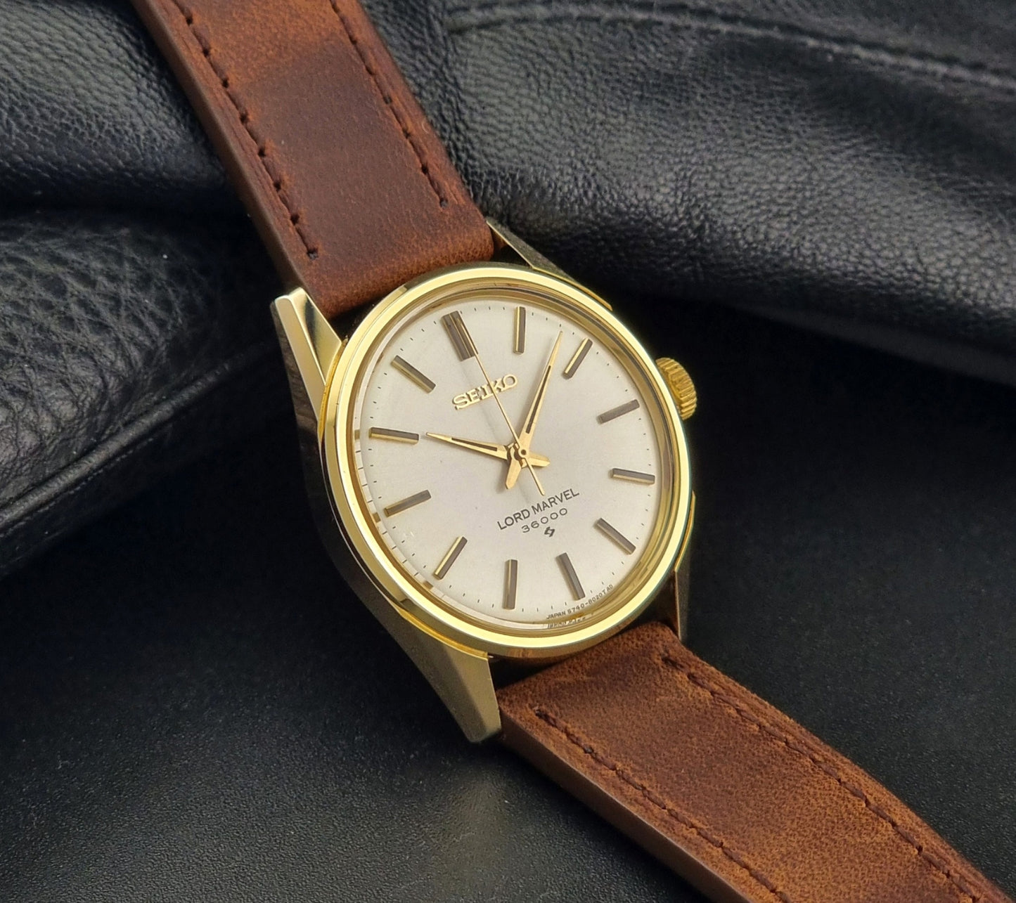 Vintage Seiko Lord Marvel 5740-8000 gold watch with a brown leather strap on a dark gray background side view