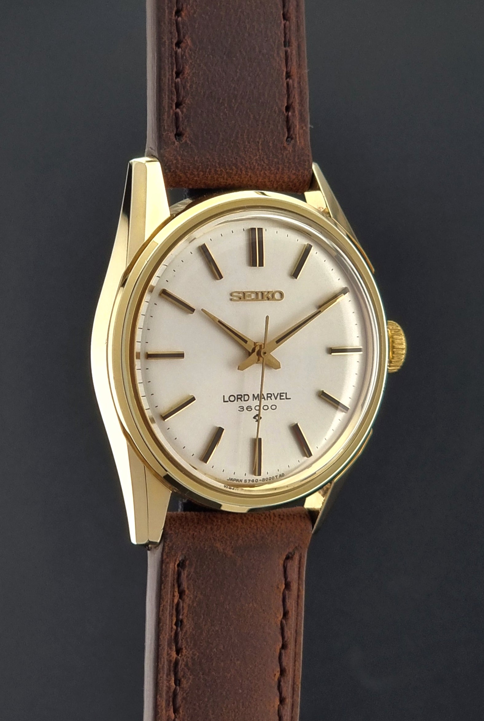 Vintage Seiko Lord Marvel 5740-8000 gold watch with a brown leather strap on a dark gray background side profile