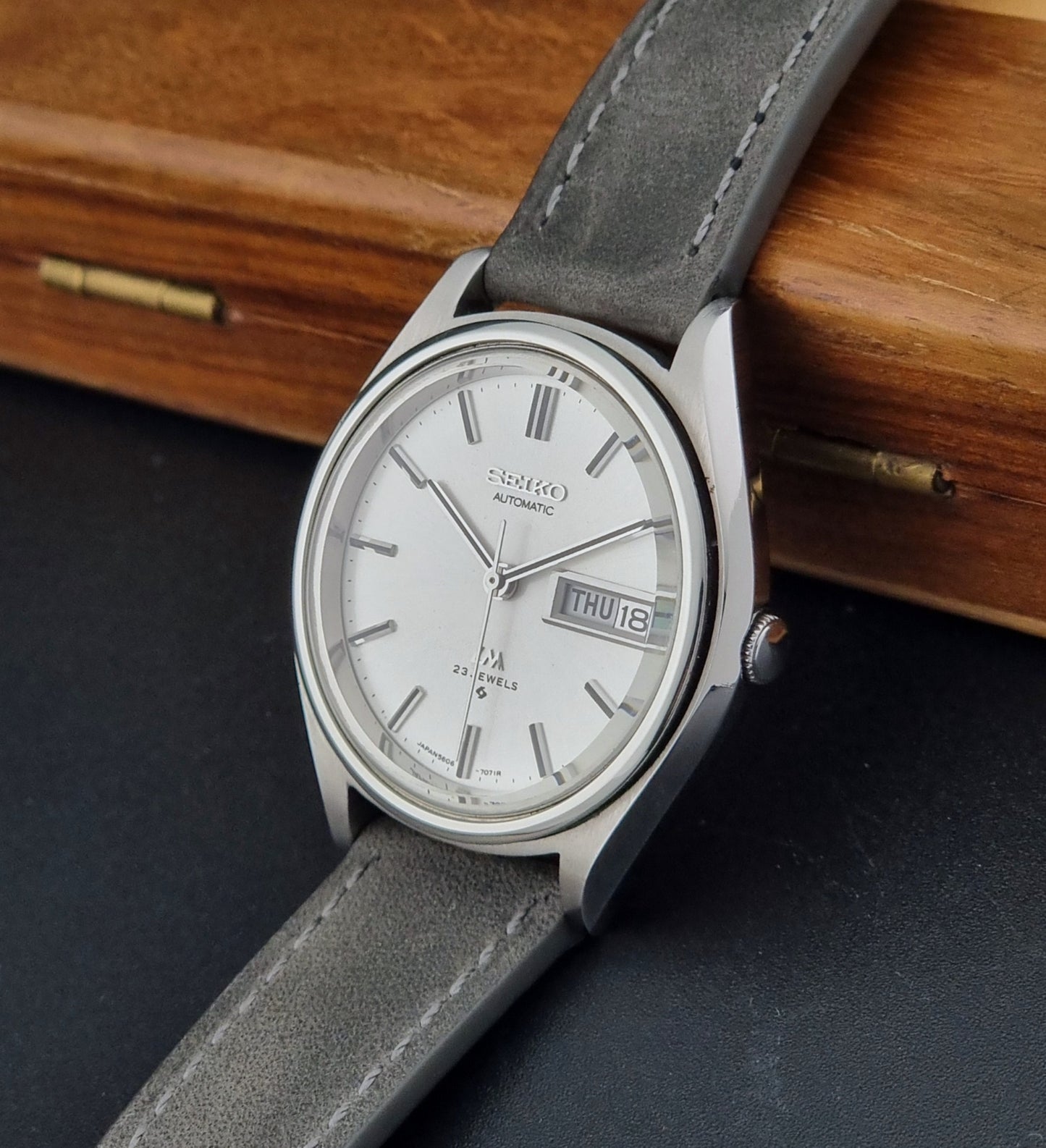 Vintage Seiko Lordmatic 5606-7071 Wristwatch with gray strap on a dark surface with wooden background