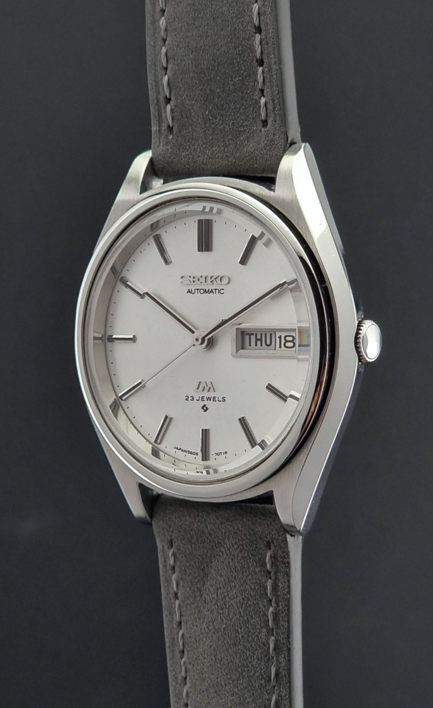 Vintage Seiko Lordmatic 5606-7071 Wristwatch with a silver case and gray leather strap on a dark background