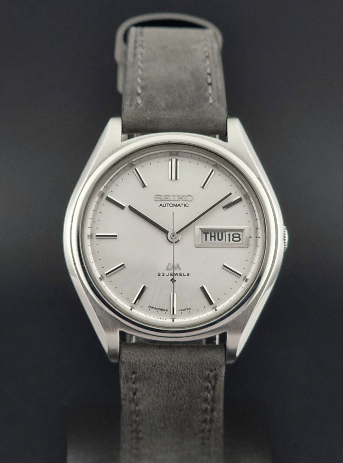 Vintage Seiko Lordmatic 5606-7071 Wristwatch with gray leather strap and silver case on a dark background