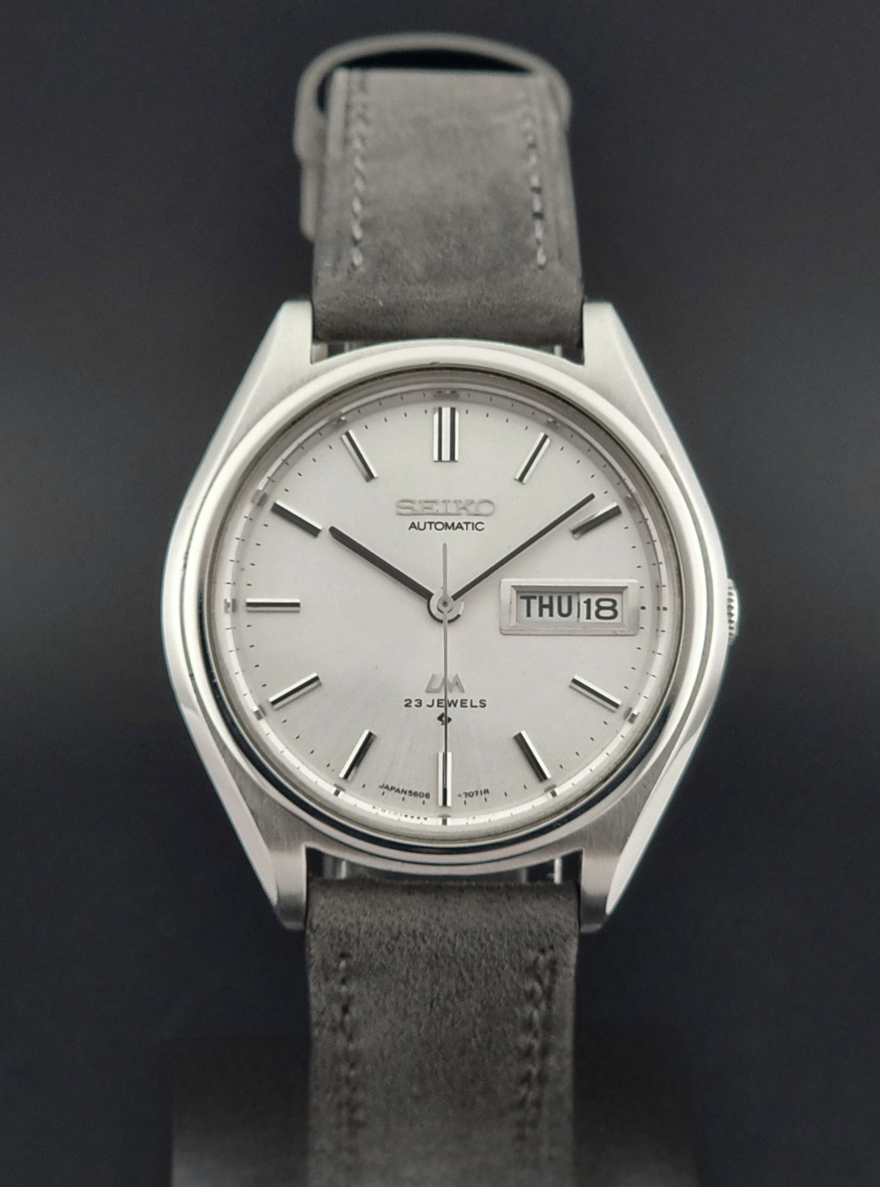 Vintage Seiko Lordmatic 5606-7071 Wristwatch with gray leather strap and silver case on a dark background