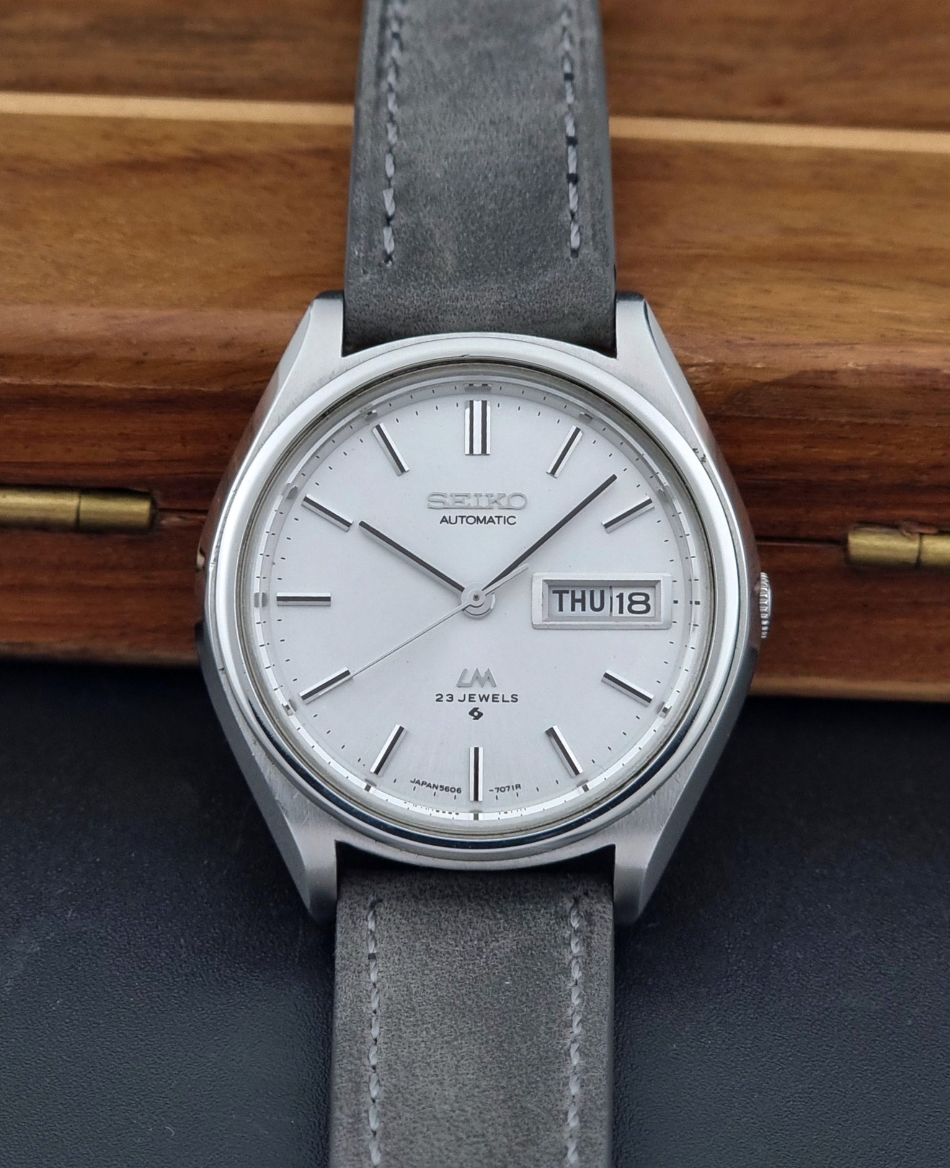 Vintage Seiko Lordmatic 5606-7071 Wristwatch with gray strap on a wooden surface