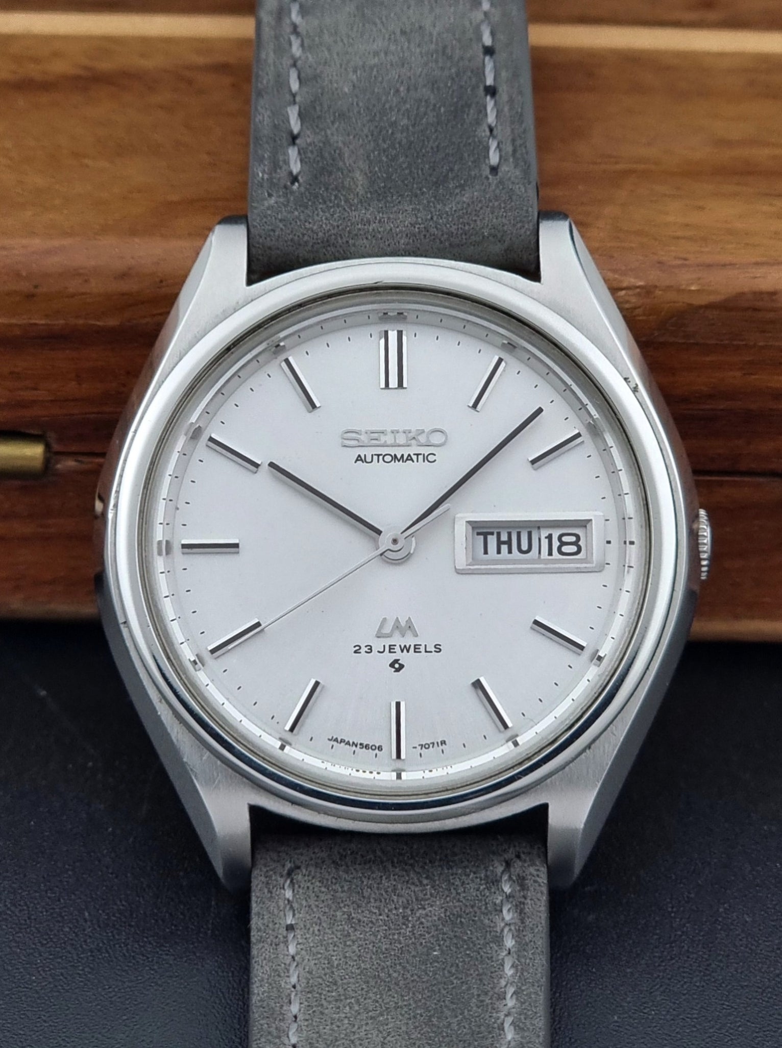 Vintage Seiko Lordmatic 5606-7071 Wristwatch with gray strap on a wooden surface
