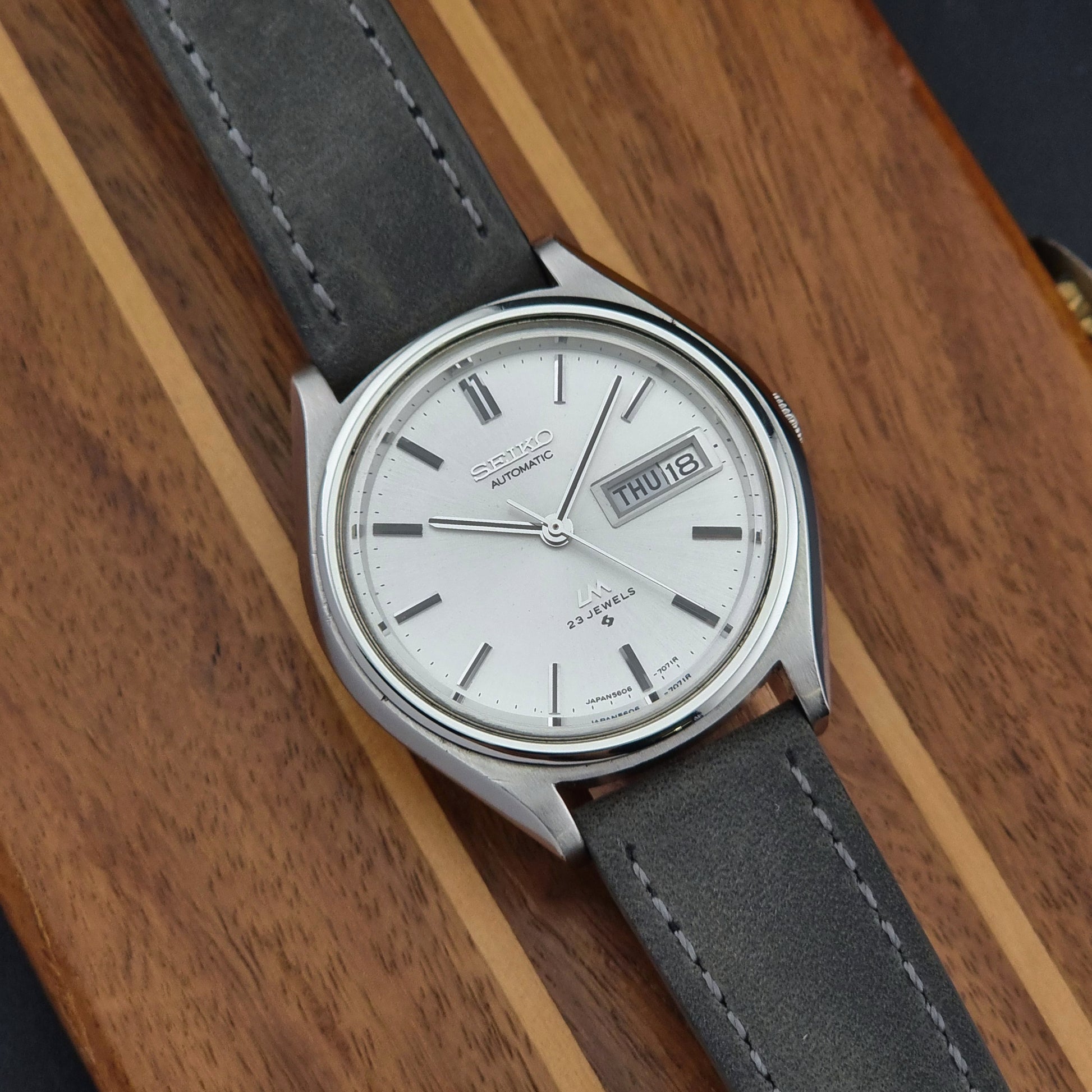 Vintage Seiko Lordmatic 5606-7071 Wristwatch with gray strap and silver case on a wooden surface
