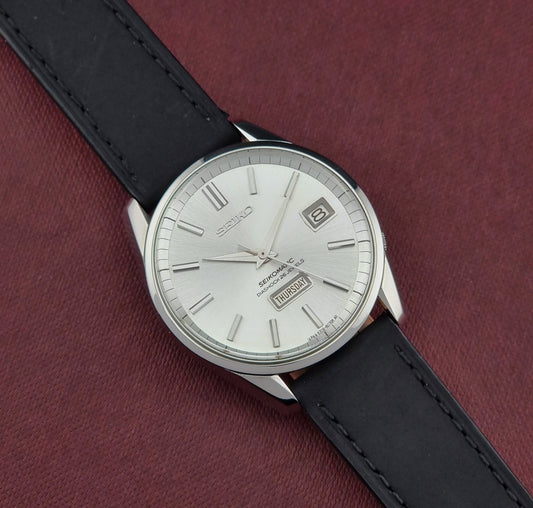 Seiko Seikomatic 6206-8040 Wristwatch with black leather strap and silver case on a maroon background