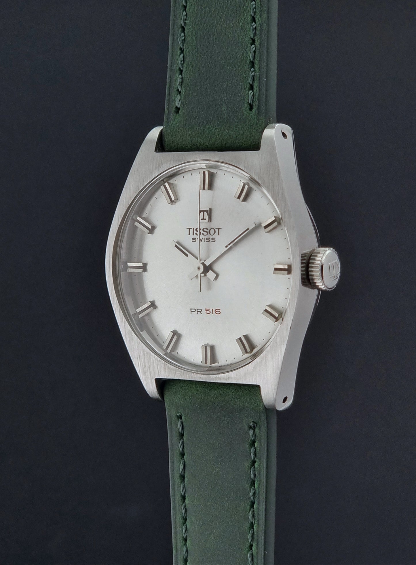 Vintage Tissot 41620 PR 516 wristwatch with green strap and silver case on a gray background crown profile view