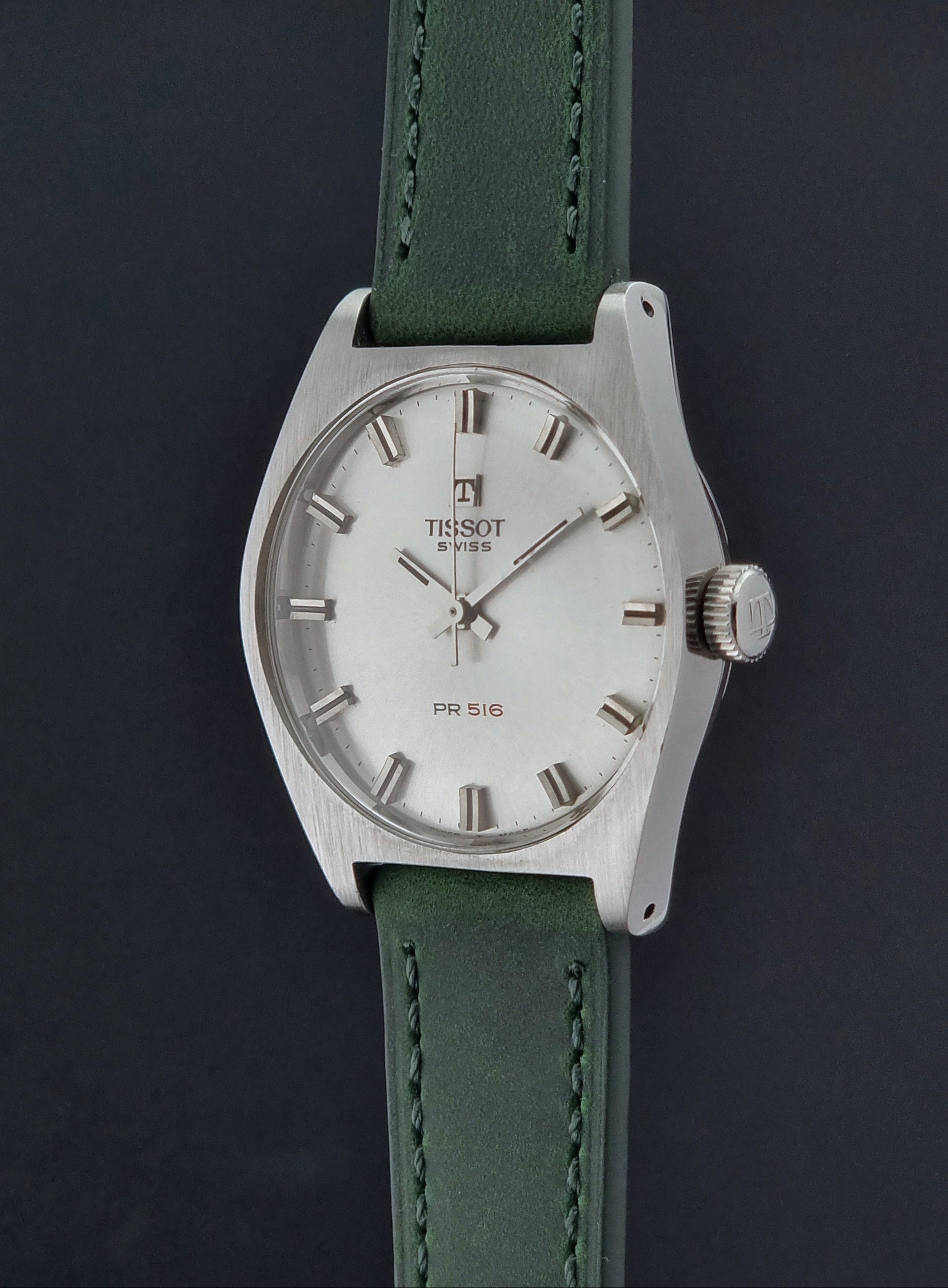 Vintage Tissot 41620 PR 516 wristwatch with green strap and silver case on a gray background crown profile view