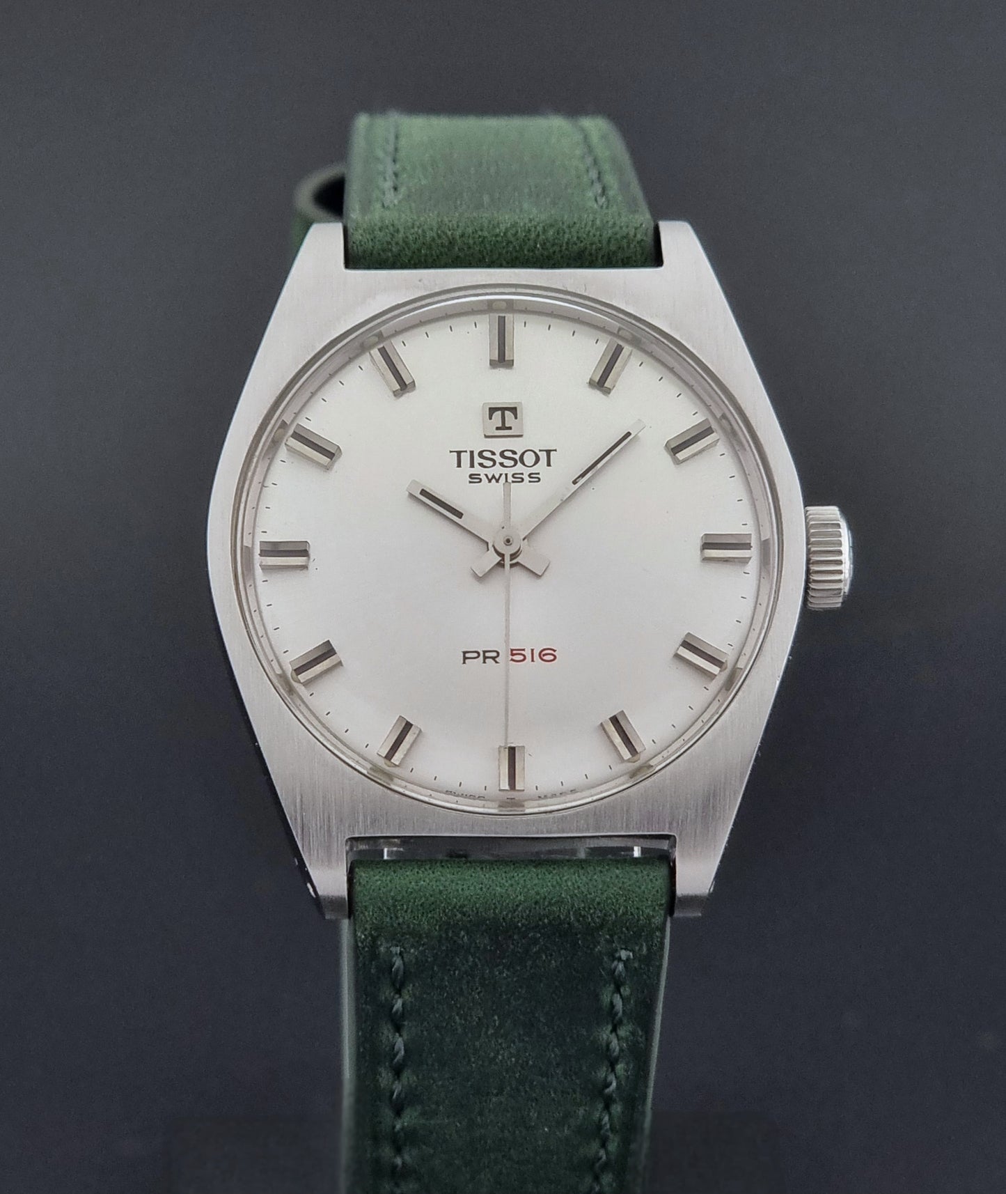 Vintage Tissot 41620 PR 516 wristwatch with green strap and silver case on a gray background close front view