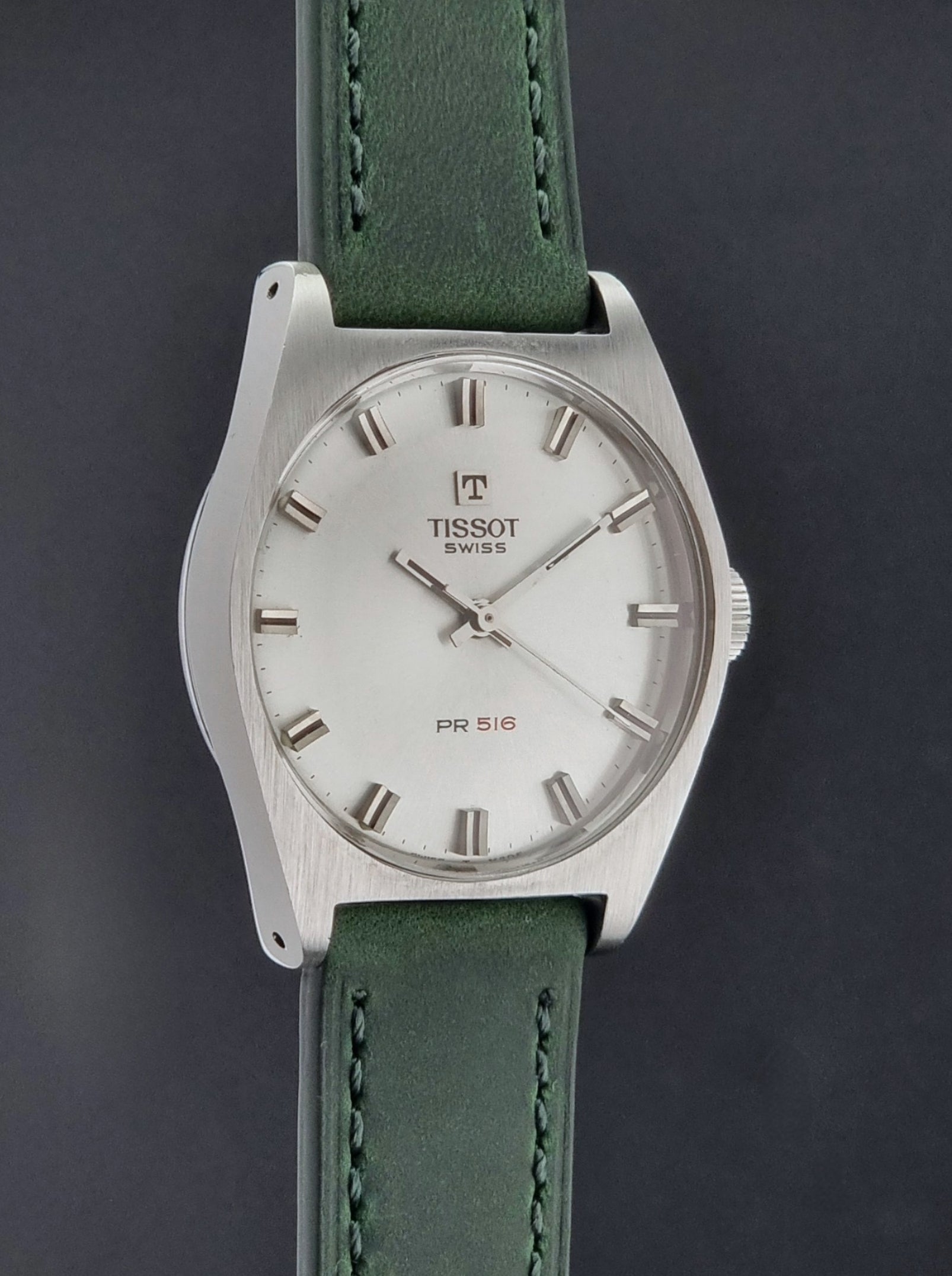 Vintage Tissot 41620 PR 516 wristwatch with green strap and silver case on a gray background side profile view