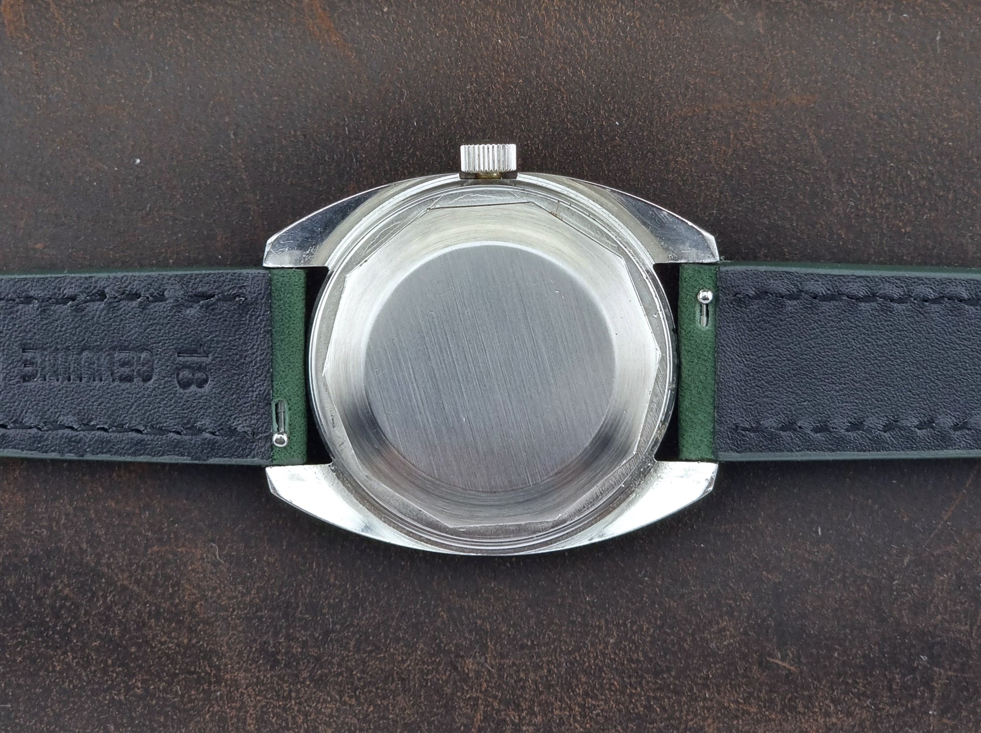 Tissot Seastar 46660 Close-up of a watch  case back with a green strap on a dark brown leather background