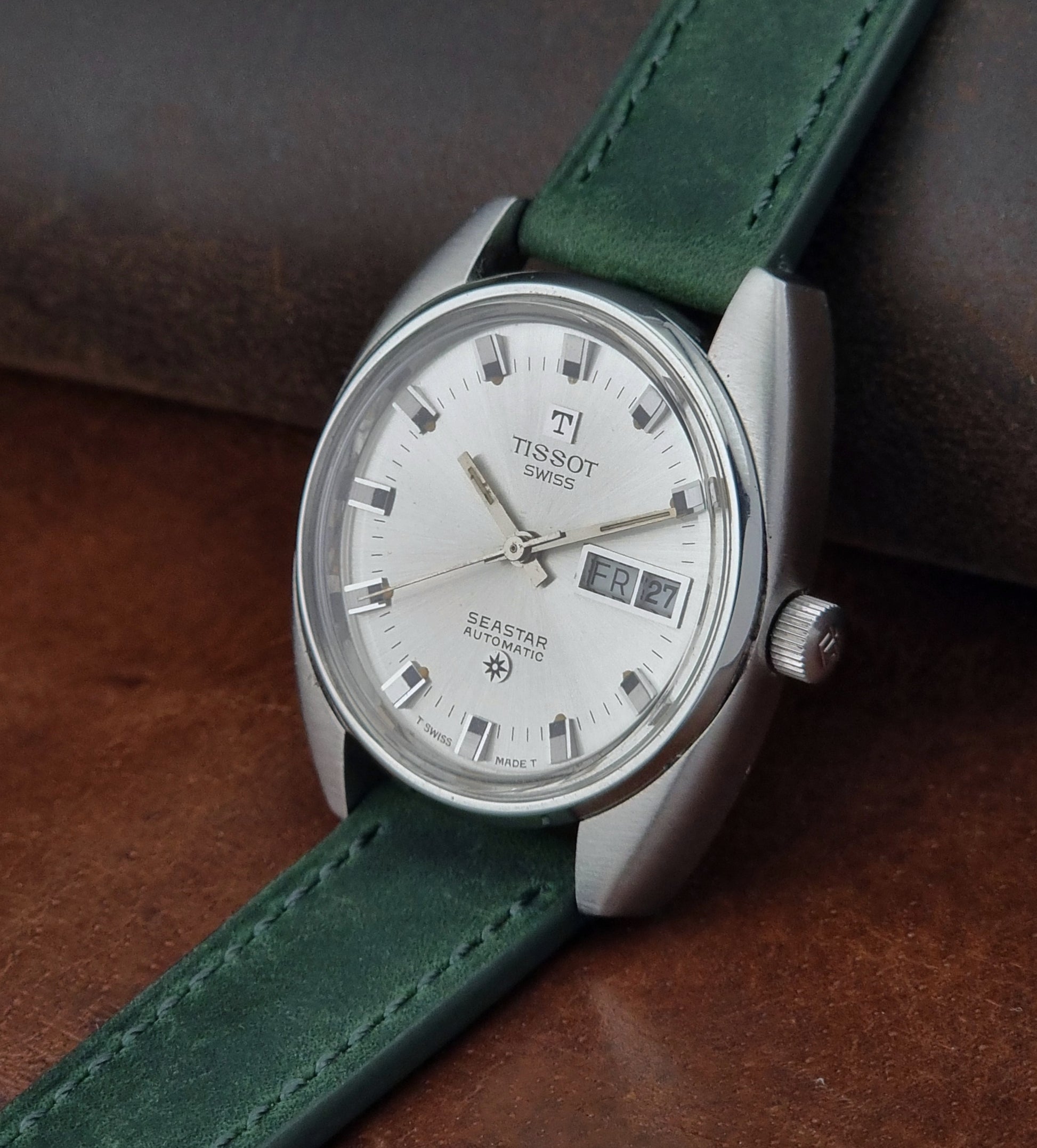 Tissot Seastar 46660 watch with green strap on a brown leather surface