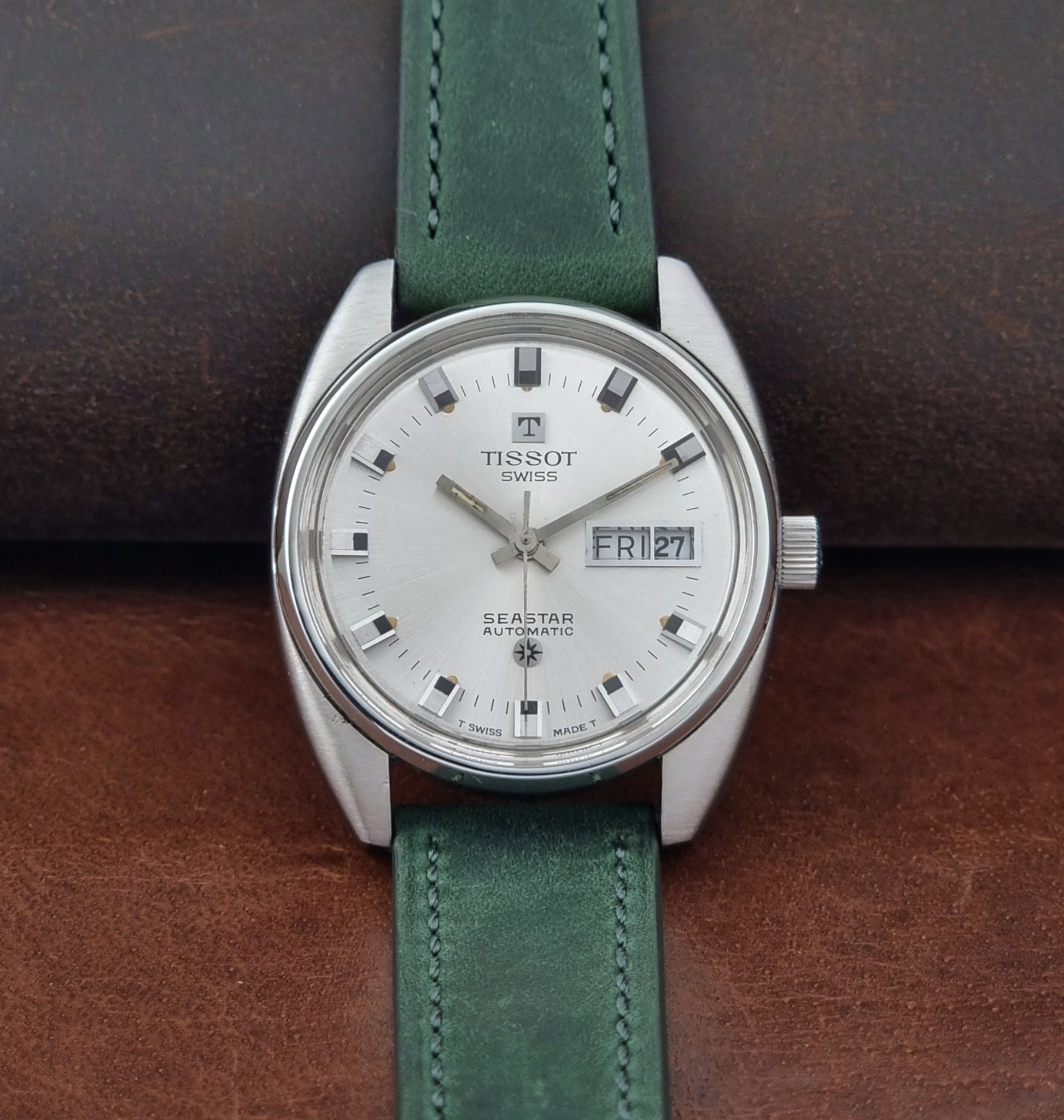 Tissot Seastar 46660 watch with green leather strap on a brown surface