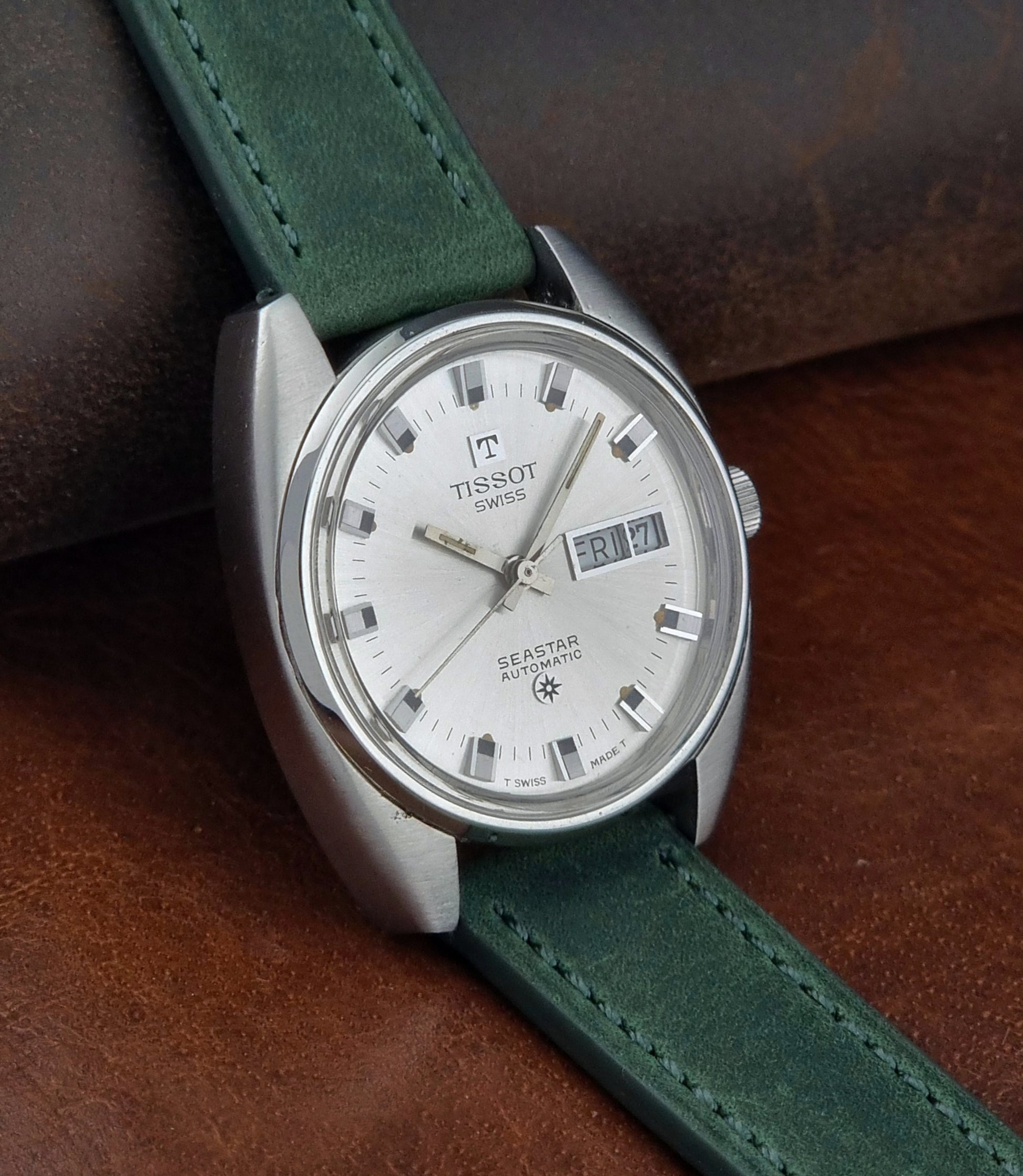 Tissot Seastar 46660 watch with green strap on a brown leather background