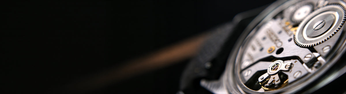 Close-up of a luxury watch with a black strap and a highly detailed, open-heart mechanical movement showing silver and gold-toned gears against a dark background.