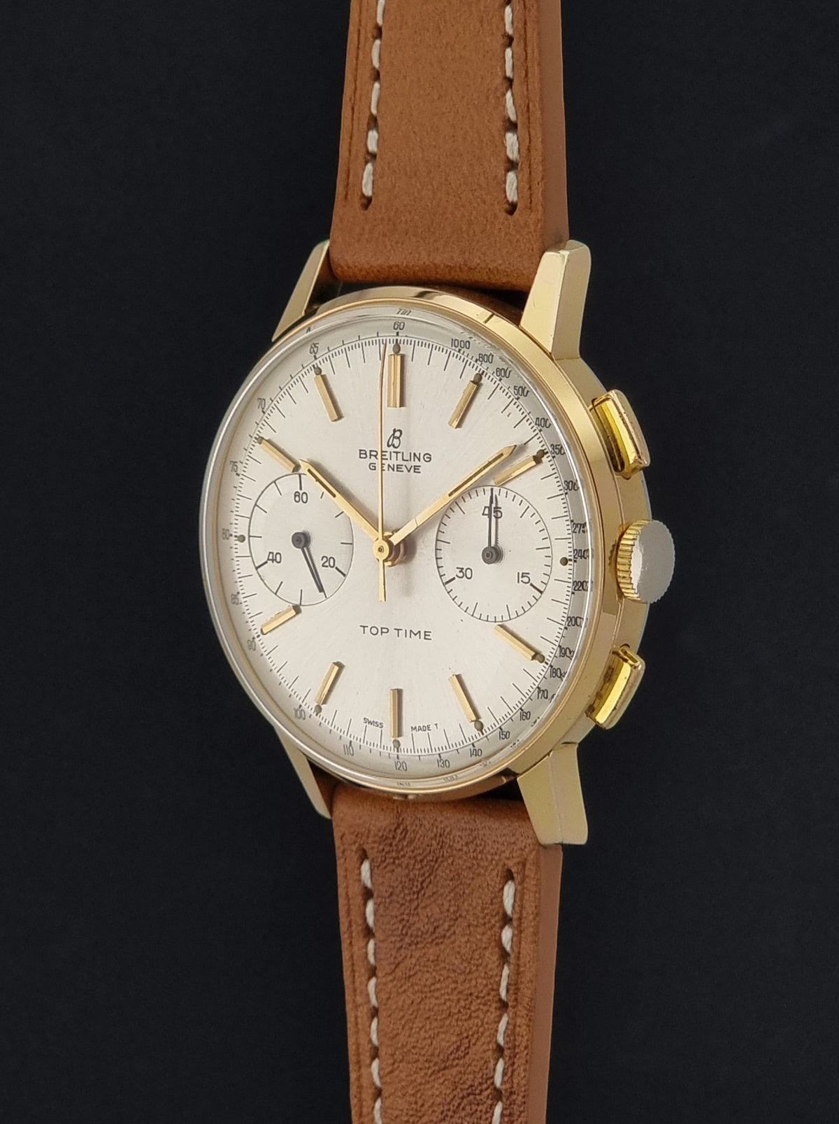 A vintage Breitling wristwatch with a gold-tone case, cream dial, and brown leather strap, shown against a dark background.