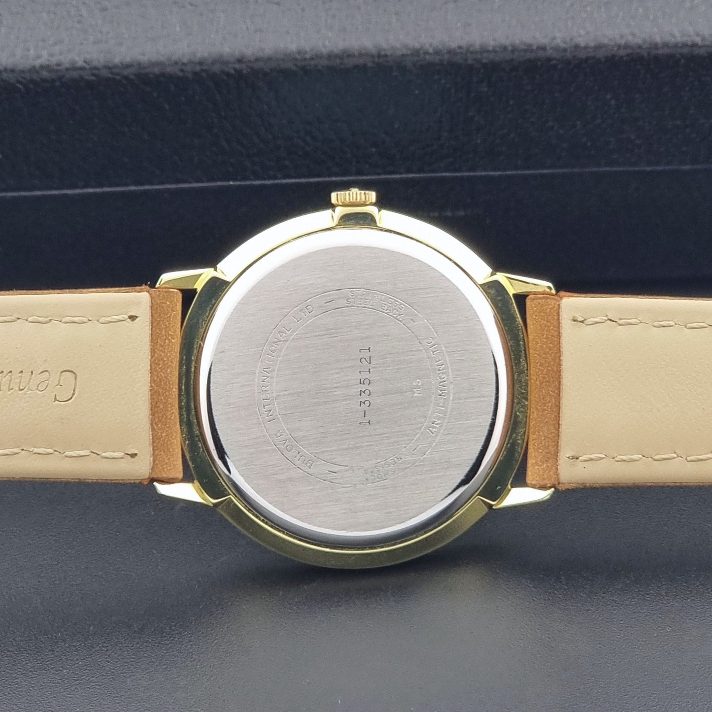 Vintage Bulova wristwatch 531  watch with a gold case, white dial, and a tan leather strap on a dark background case back view
