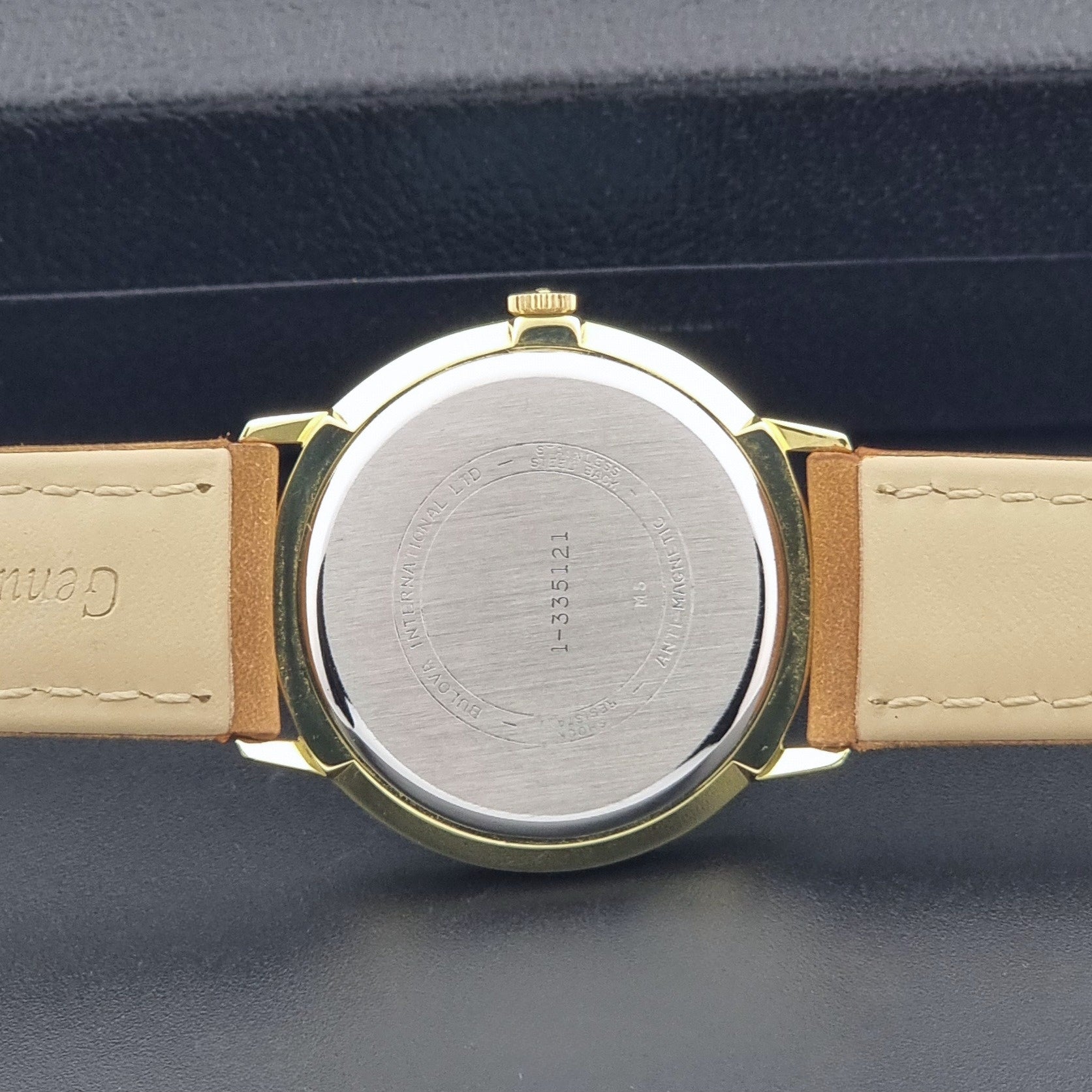 Vintage Bulova wristwatch 531  watch with a gold case, white dial, and a tan leather strap on a dark background case back view
