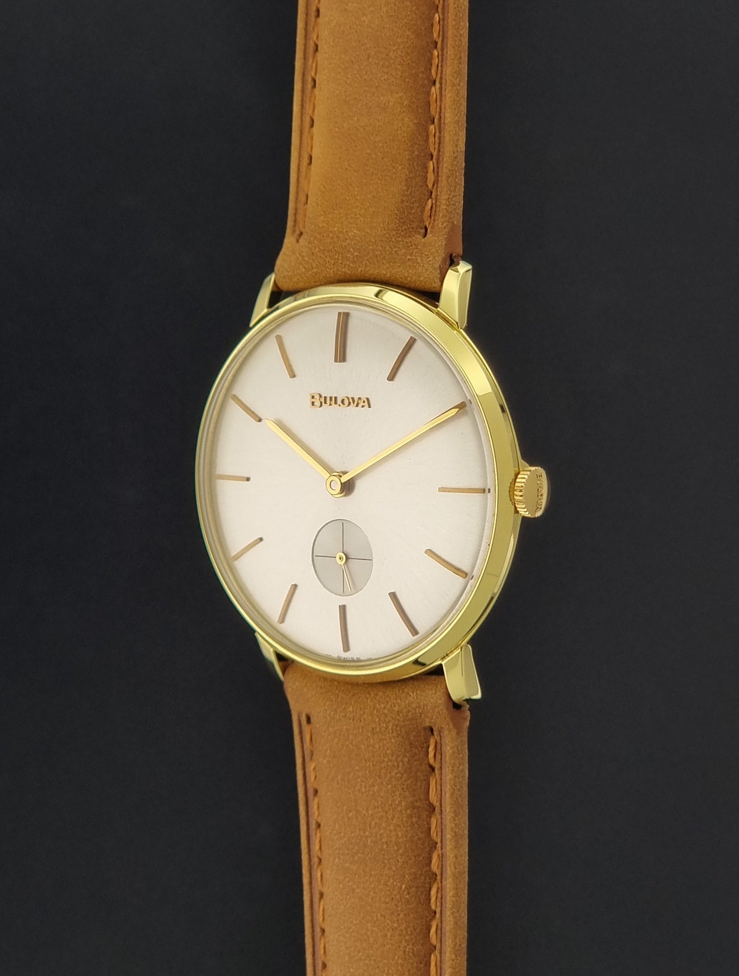Vintage Bulova wristwatch 531  watch with a gold case, white dial, and a tan leather strap on a dark background crown profile view