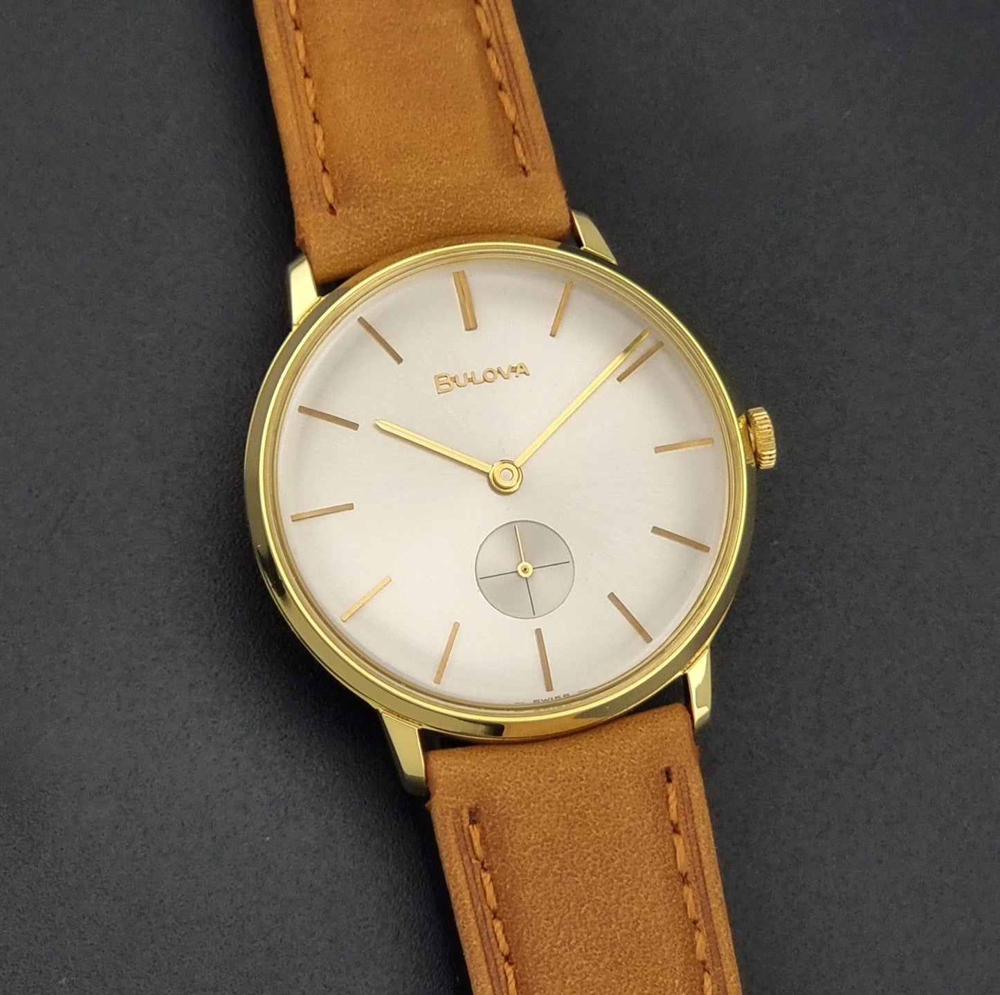 Vintage Bulova wristwatch 531  watch with a gold case, white dial, and a tan leather strap on a dark background front view