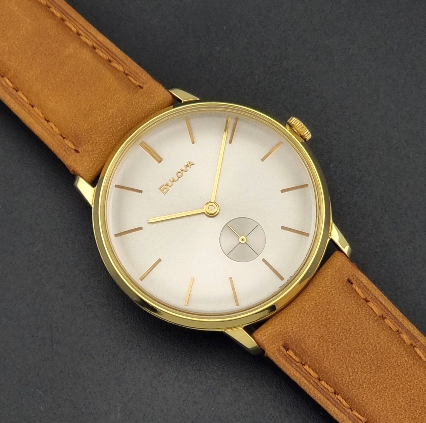Vintage Bulova wristwatch 531  watch with a gold case, white dial, and a tan leather strap on a dark background close up dial view