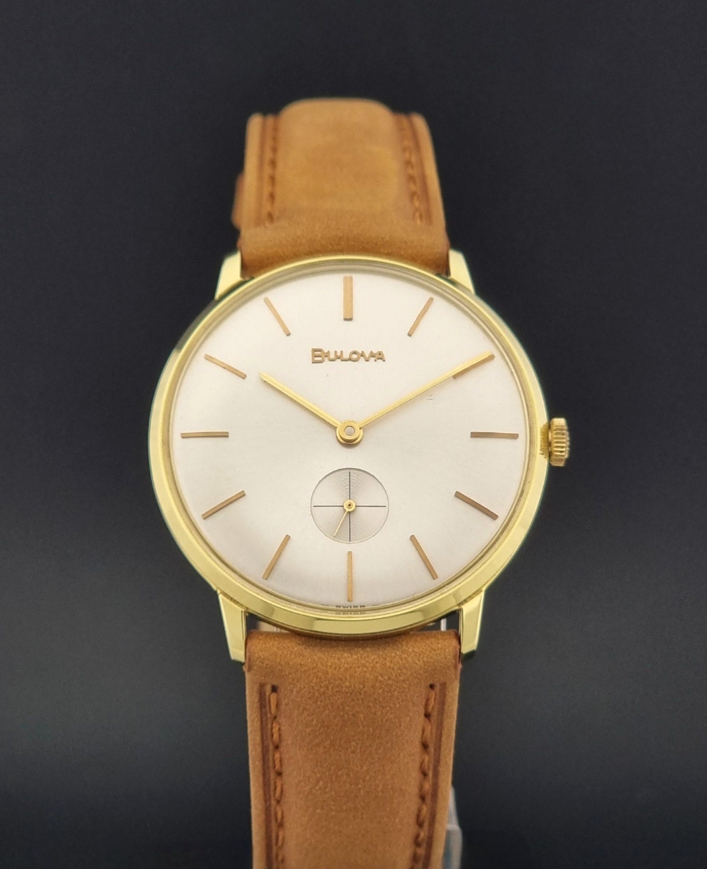 Vintage Bulova wristwatch 531  watch with a gold case, white dial, and a tan leather strap on a dark background close dial view