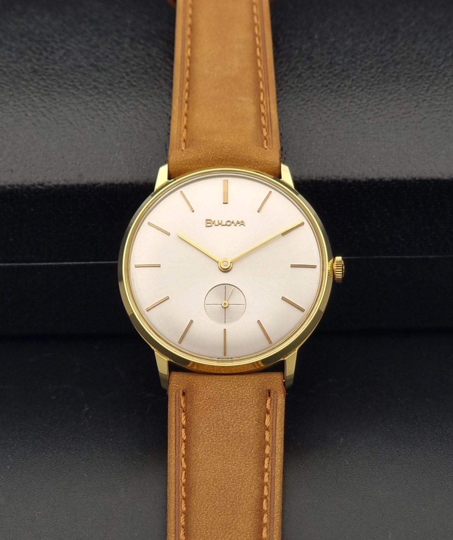 Vintage Bulova wristwatch 531  watch with a gold case, white dial, and a tan leather strap on a dark background dial view