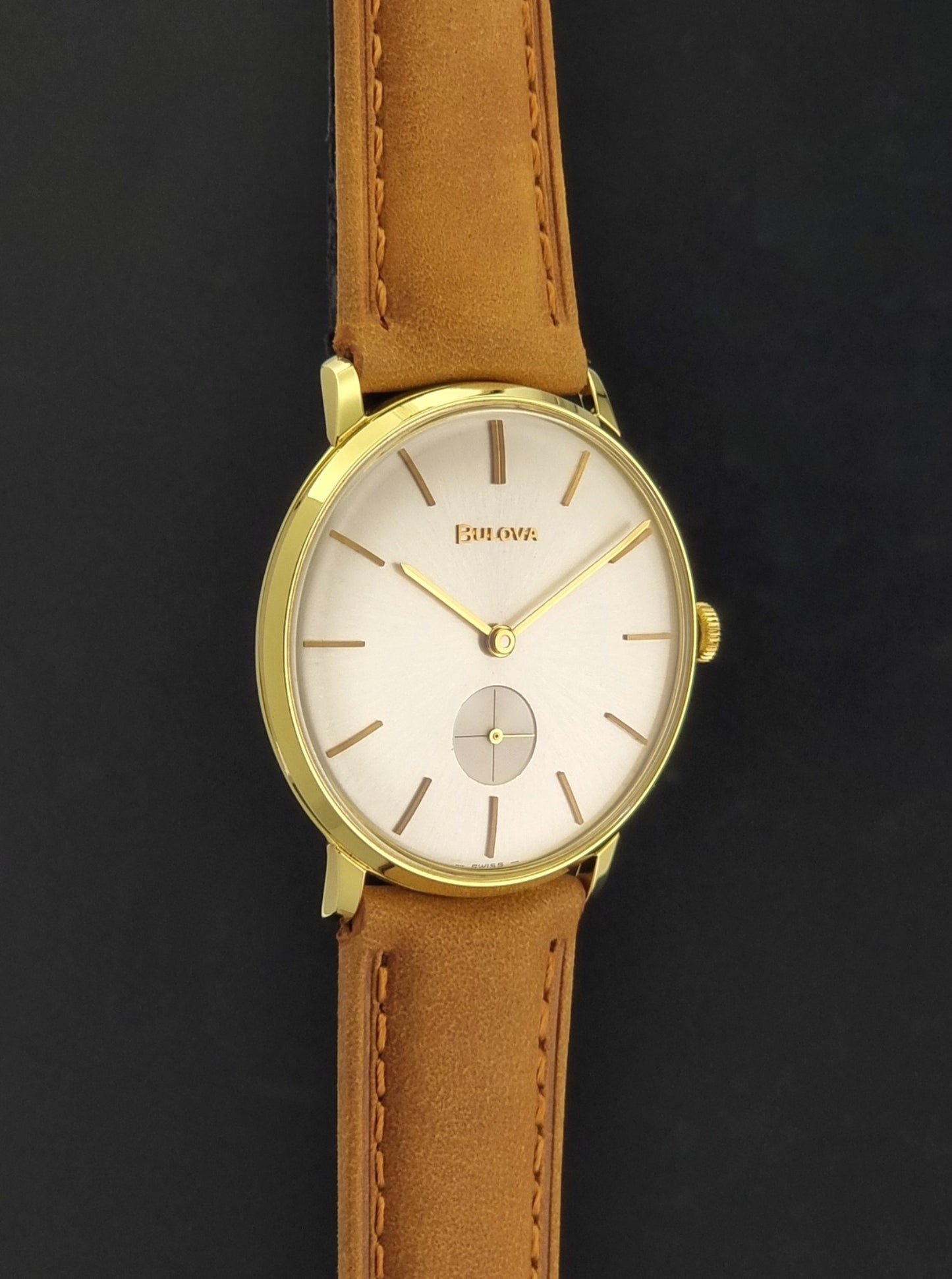 Vintage Bulova wristwatch 531  watch with a gold case, white dial, and a tan leather strap on a dark background side profile view