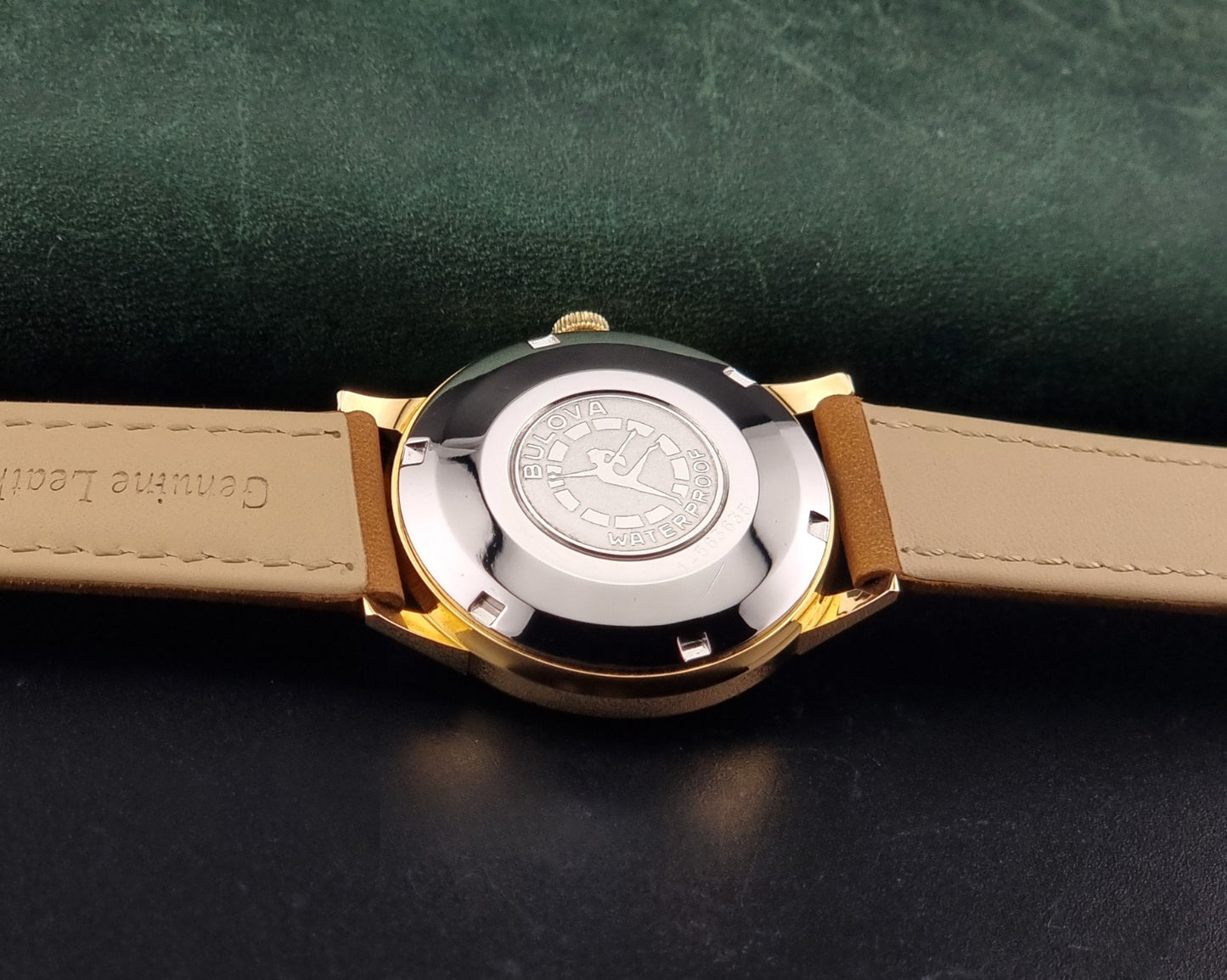 Vintage Bulova wristwatch 576-1  watch with a gold case, white dial, and a tan leather strap on a dark background case back view