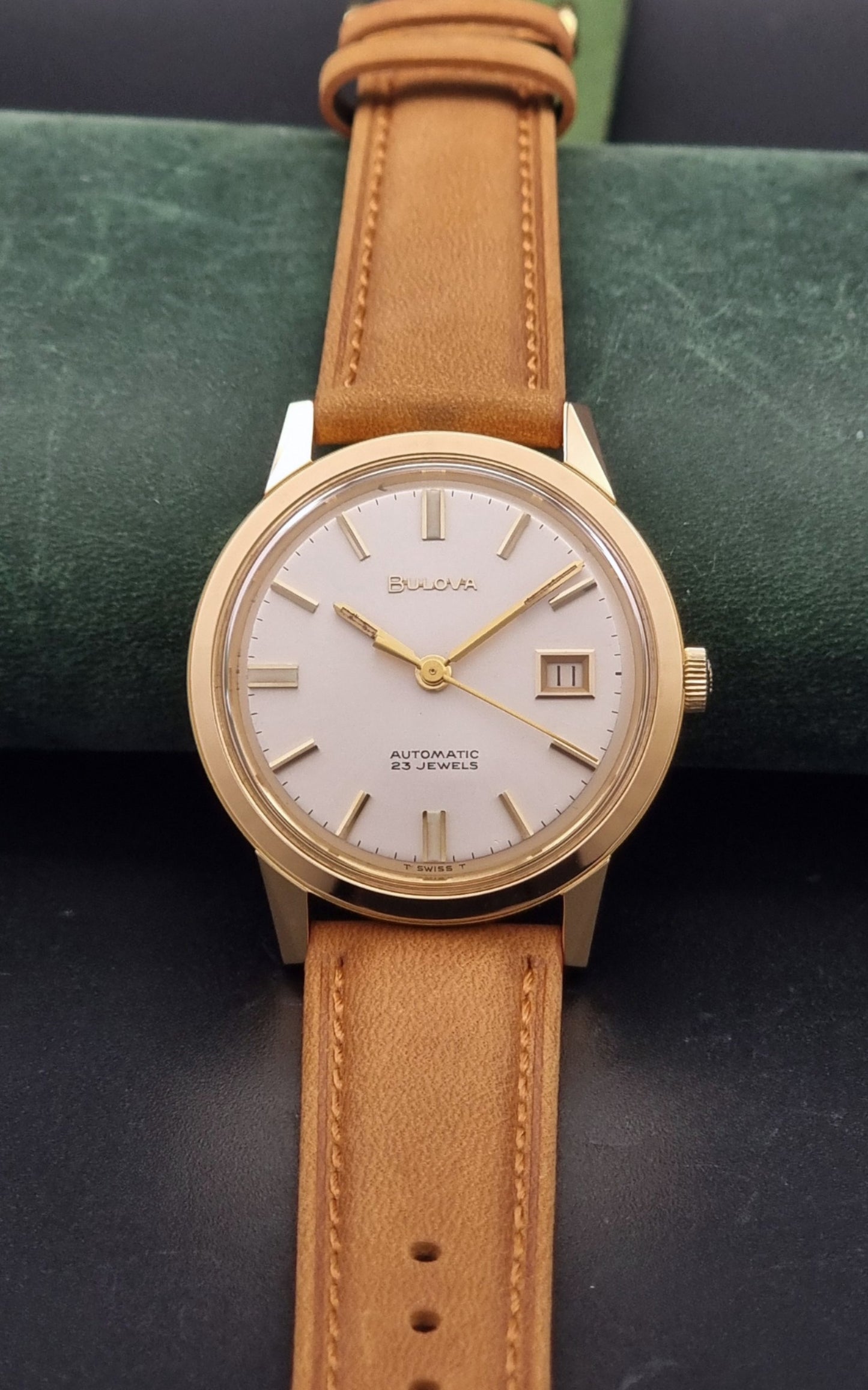 Vintage Bulova wristwatch 576-1  watch with a gold case, white dial, and a tan leather strap on a dark background close dial view