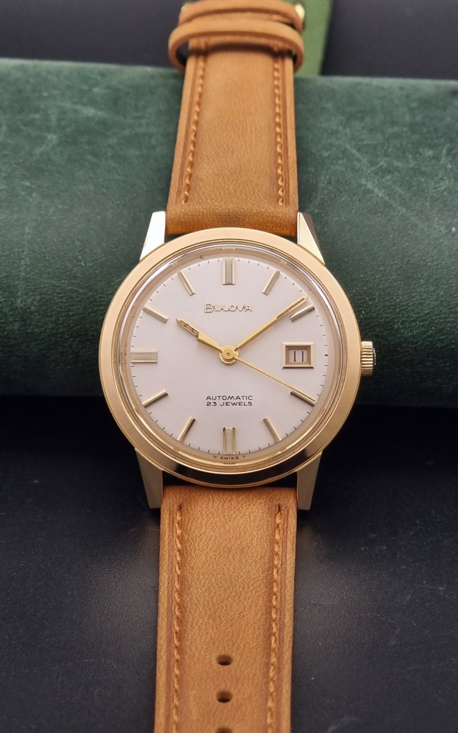 Vintage Bulova wristwatch 576-1  watch with a gold case, white dial, and a tan leather strap on a dark background close dial view