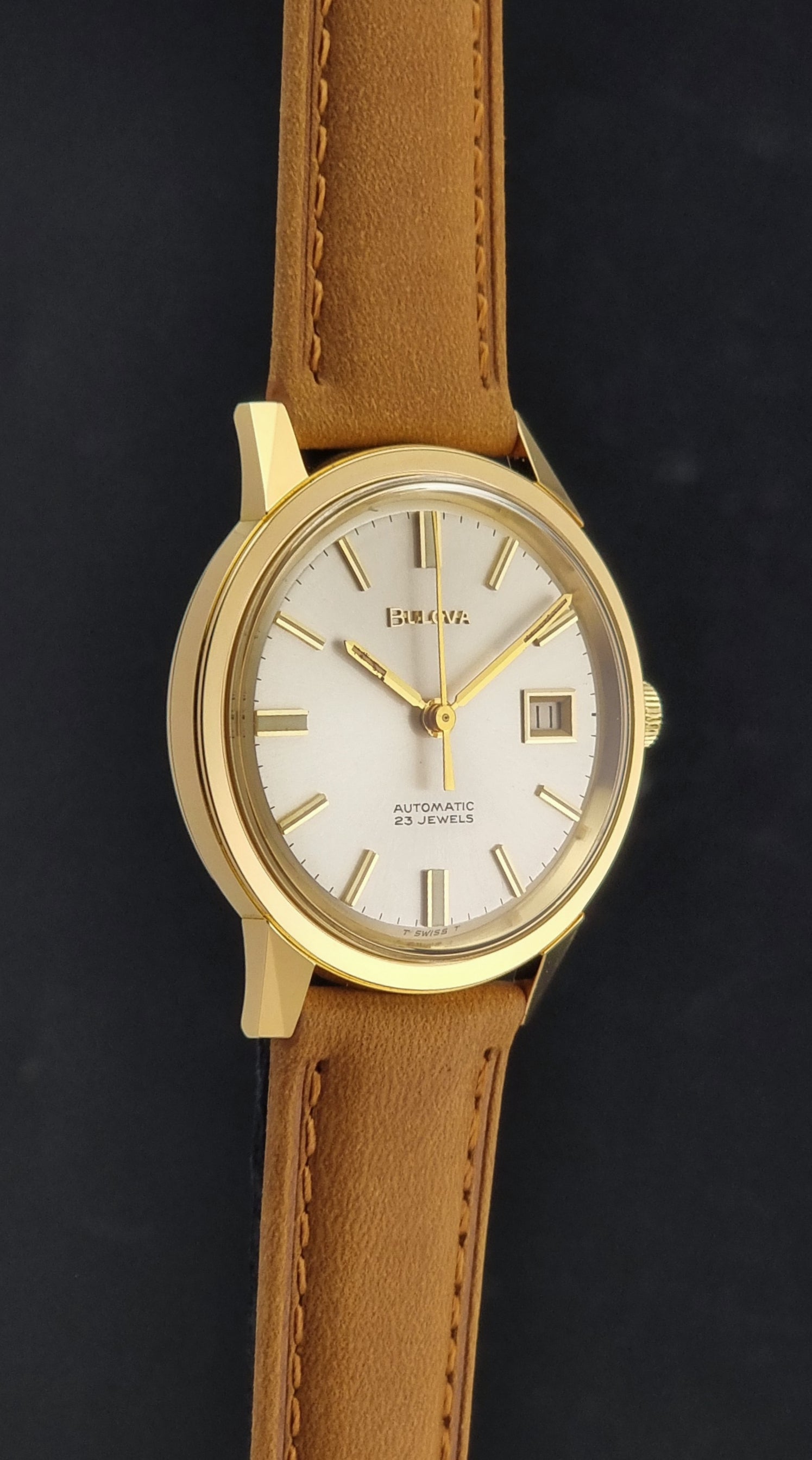 Vintage Bulova wristwatch 576-1  watch with a gold case, white dial, and a tan leather strap on a dark background side profile view