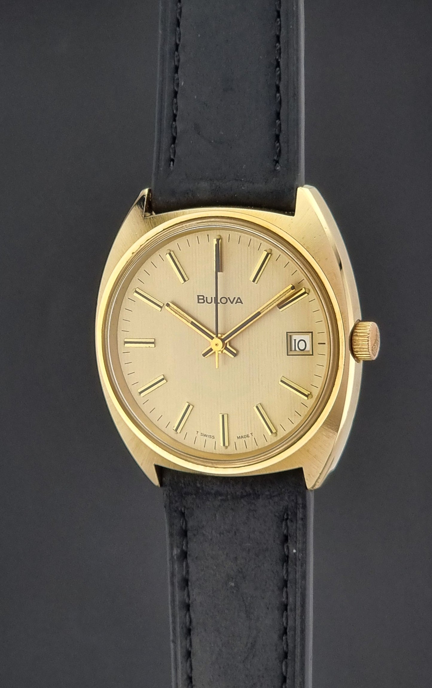 Vintage Bulova wristwatch 7530-1 with black leather strap on a gray surface crown profile view