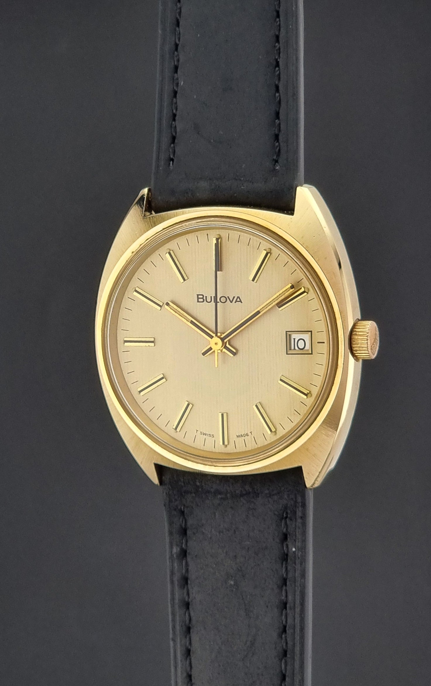 Vintage Bulova wristwatch 7530-1 with black leather strap on a gray surface crown profile view