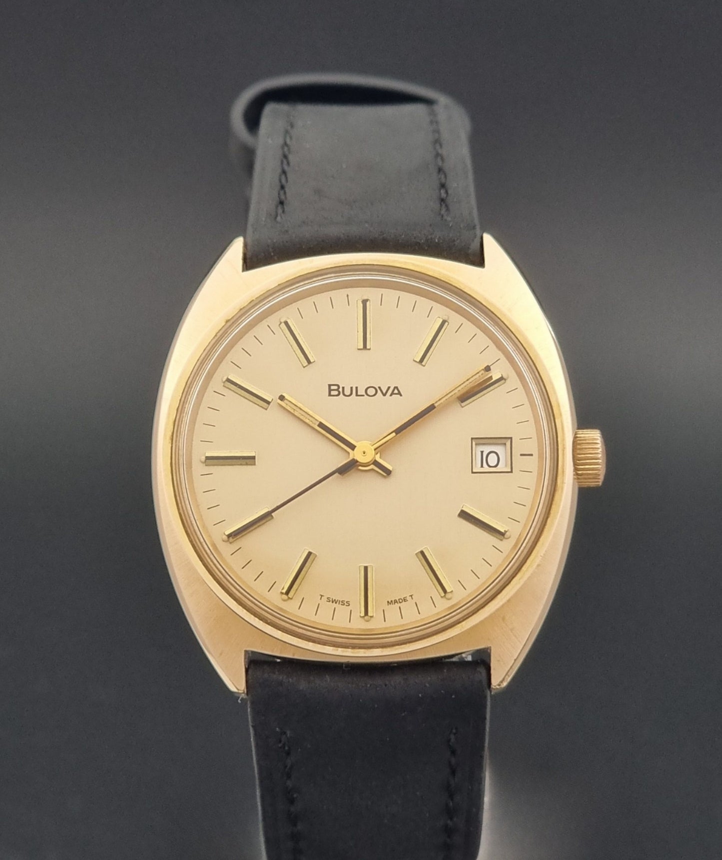 Vintage Bulova wristwatch 7530-1 with black leather strap on a gray surface close dial view