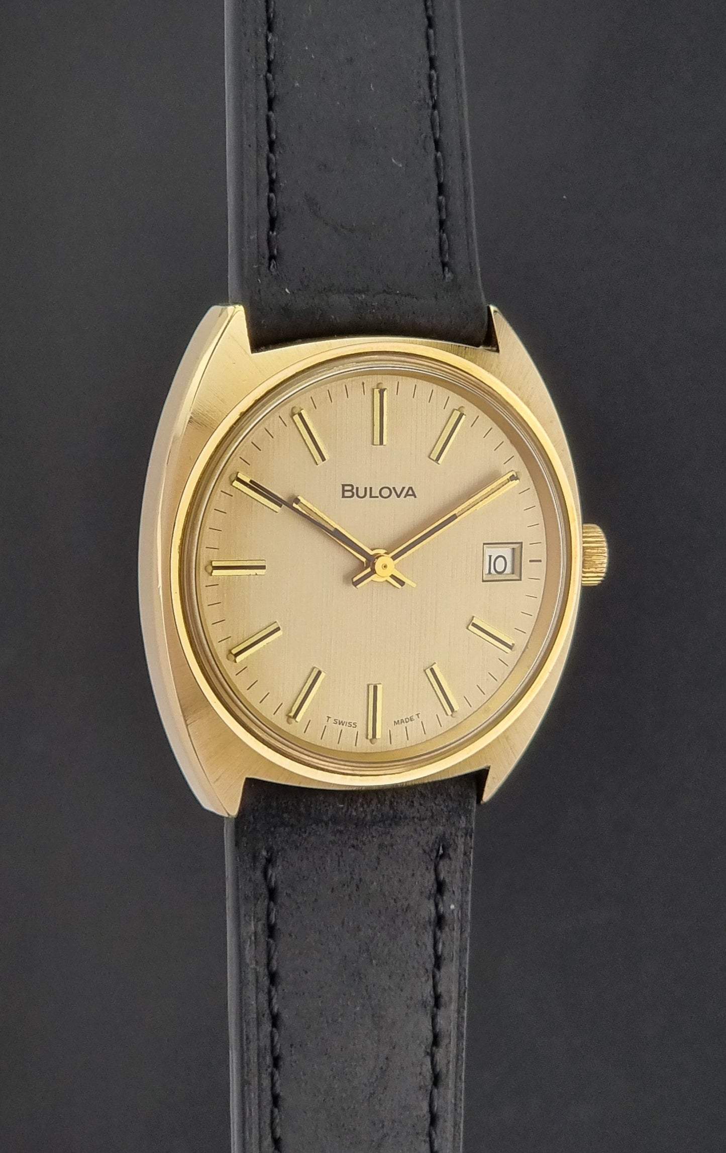 Vintage Bulova wristwatch 7530-1 with black leather strap on a gray surface side profile view