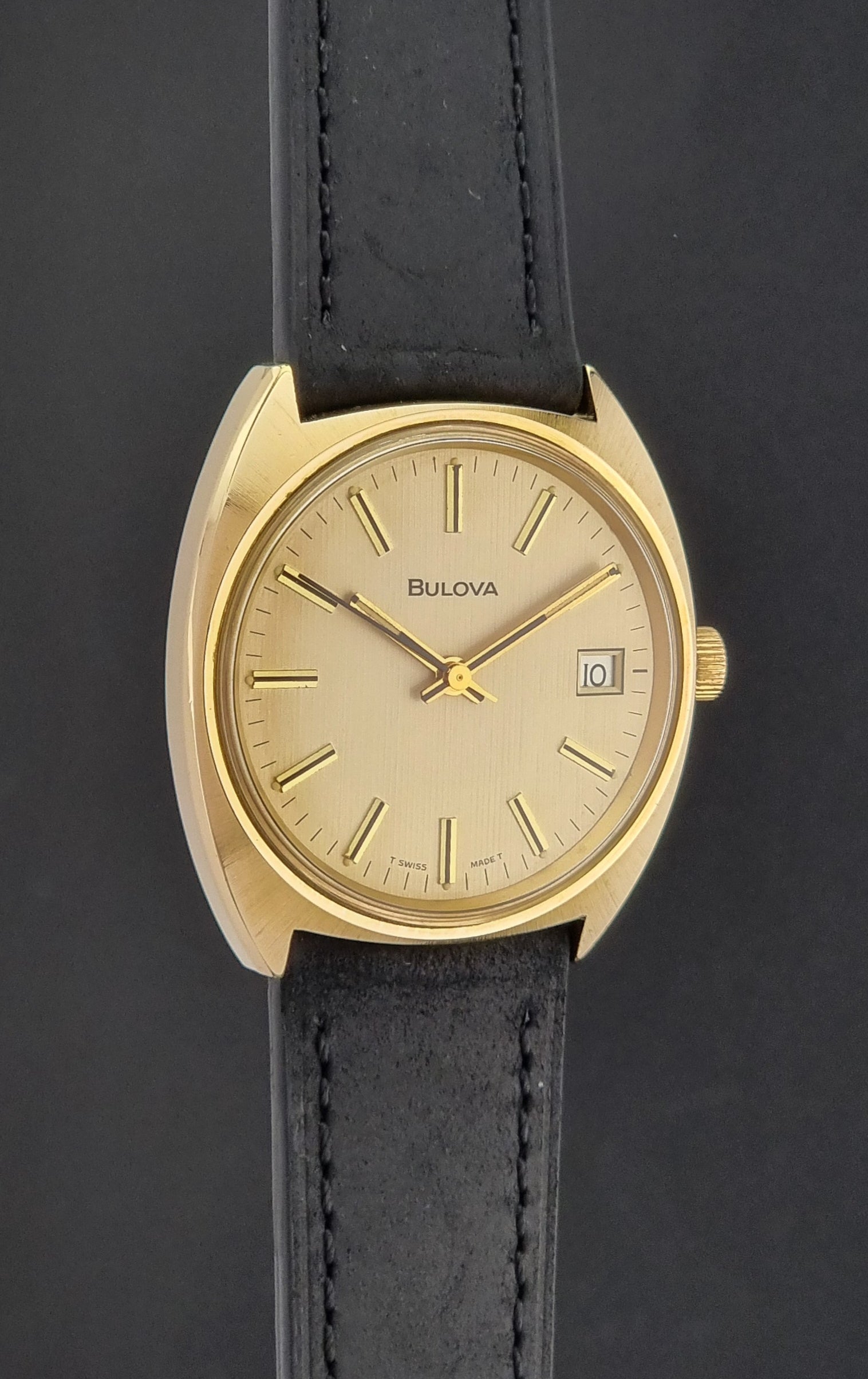 Vintage Bulova wristwatch 7530-1 with black leather strap on a gray surface side profile view