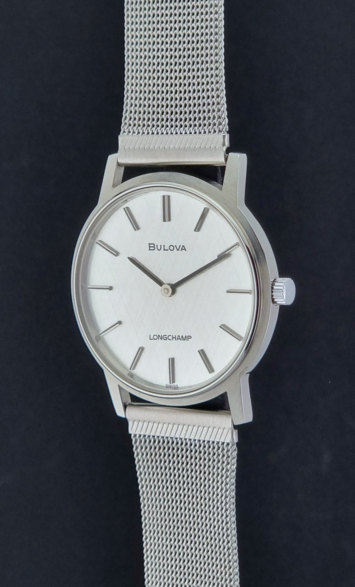Vintage Bulova 9881 wristwatch Longchamps co-signed dial with a mesh band on a dark gray background crown profile view