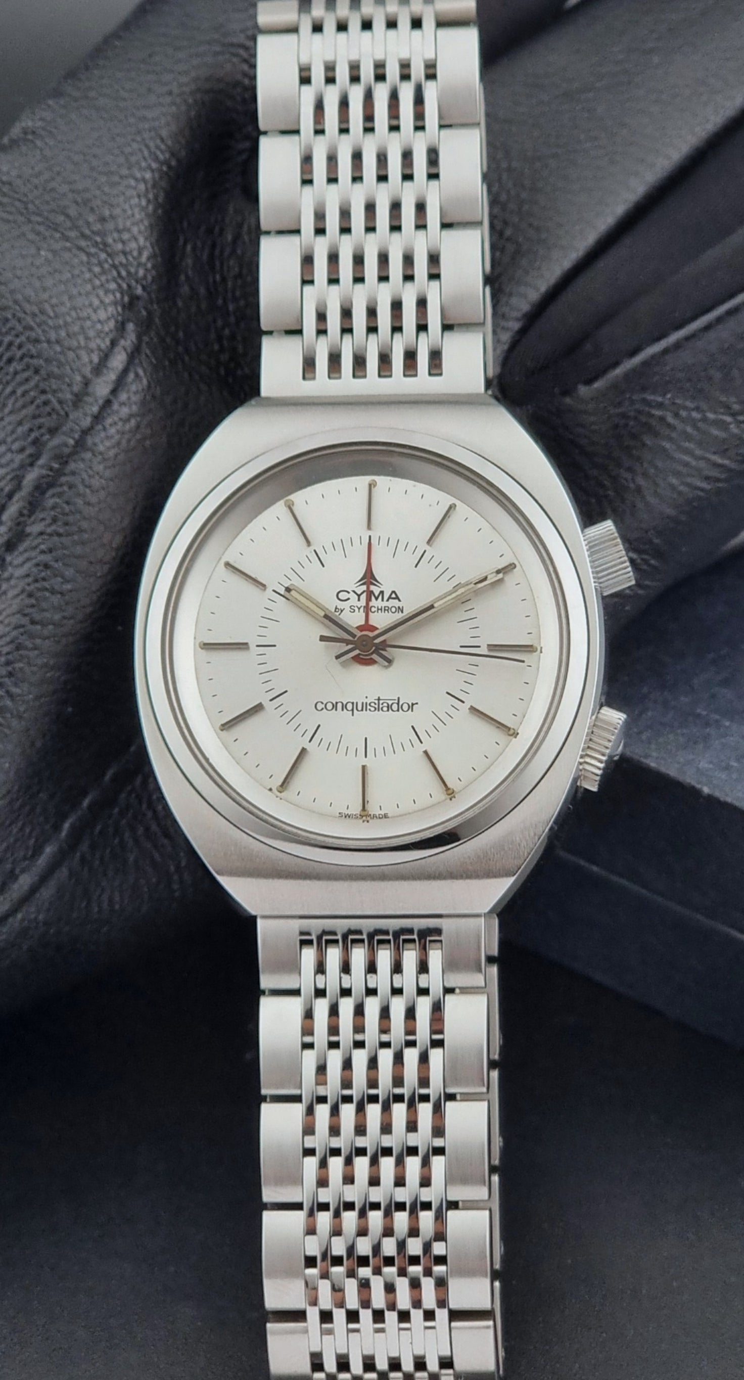 Vintage Cyma Alarm watch by Synchron a Conquistador 34270 with a detailed face on a dark surface front view