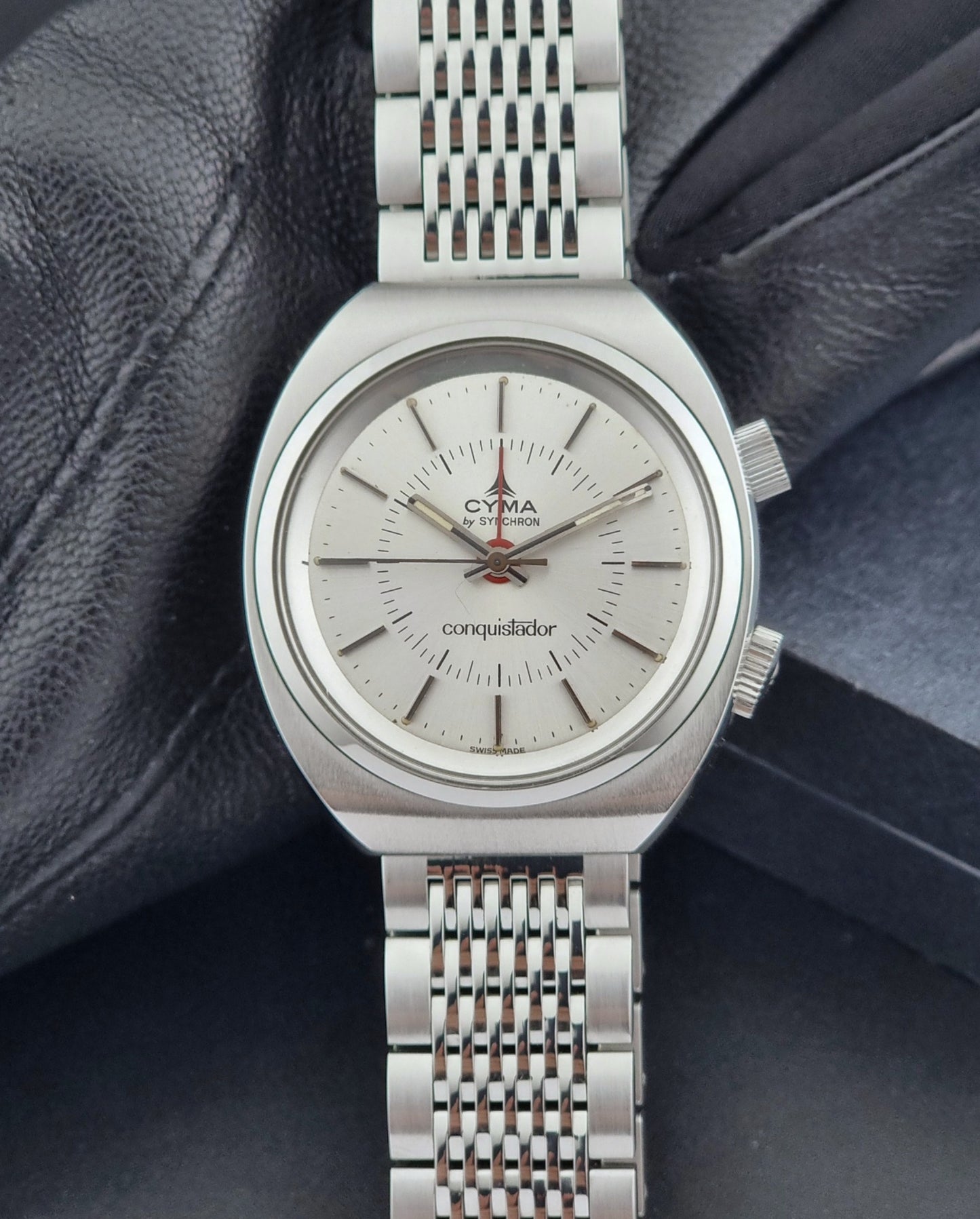 Vintage Cyma Alarm watch by Synchron a Conquistador 34270 with a detailed face on a dark surface close dial view