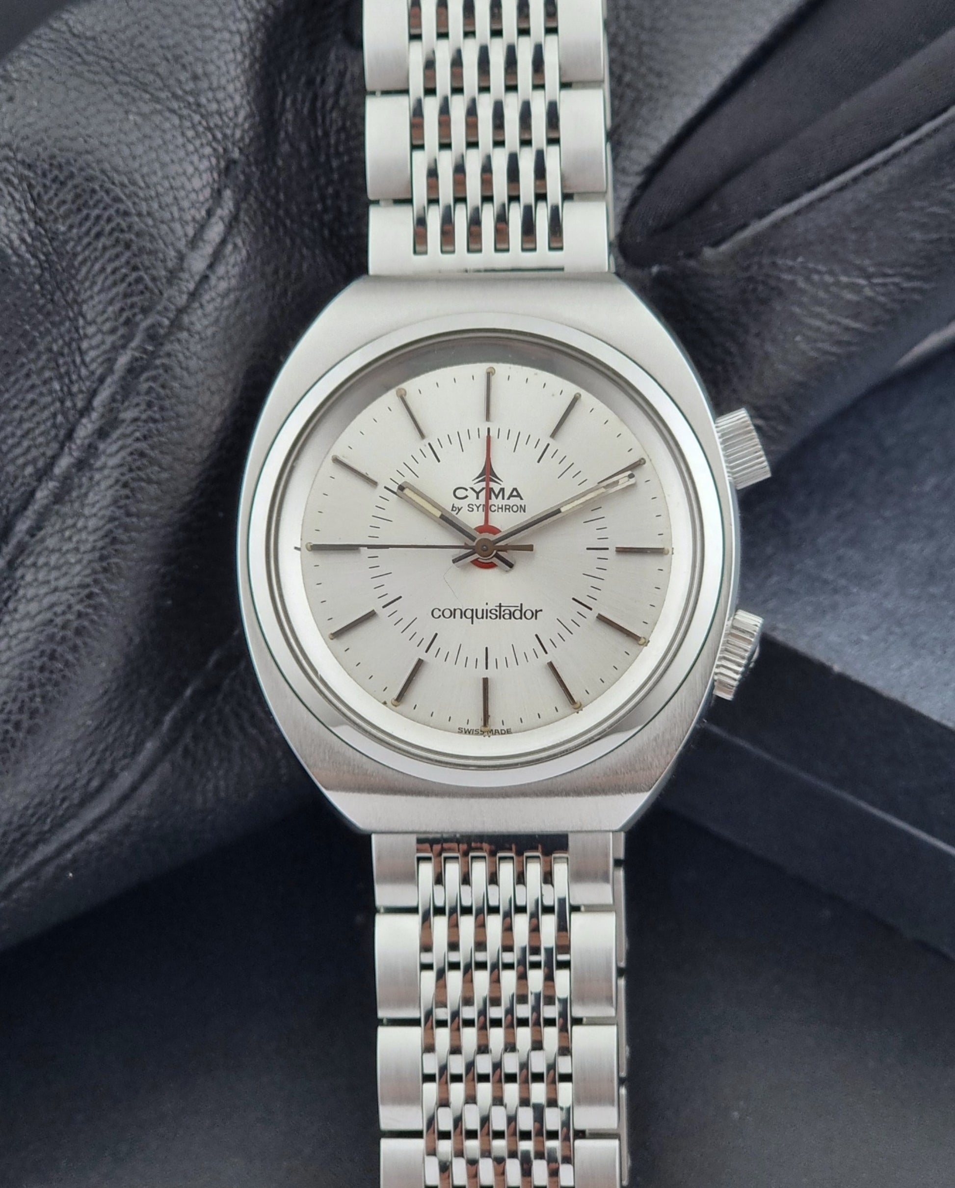 Vintage Cyma Alarm watch by Synchron a Conquistador 34270 with a detailed face on a dark surface close dial view