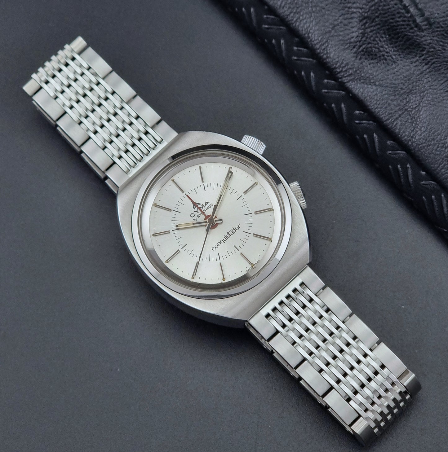 Vintage Cyma Alarm watch by Synchron a Conquistador 34270 with a detailed face on a dark surface front